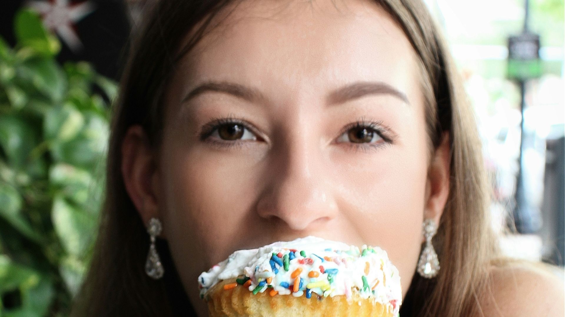Woman happily eats a large, decorated cupcake.