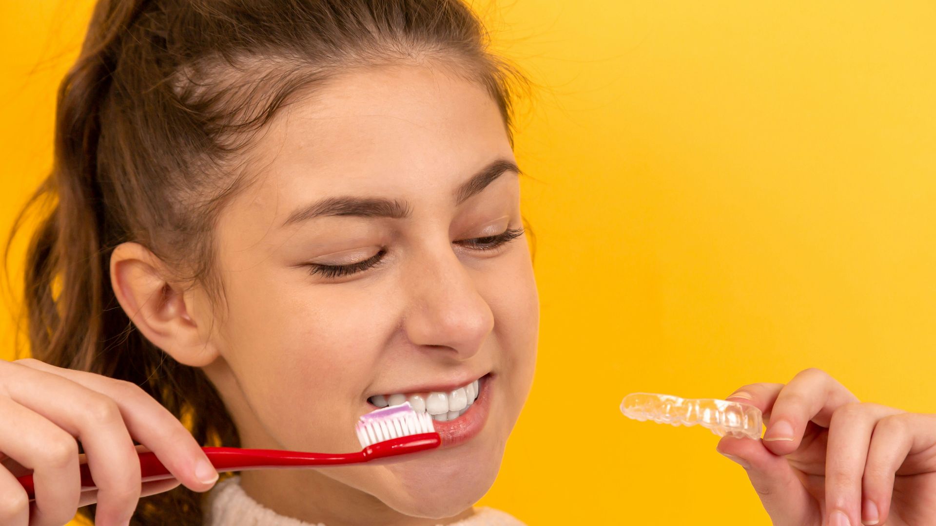 smiling girl in white sweater holding red and white toothbrush