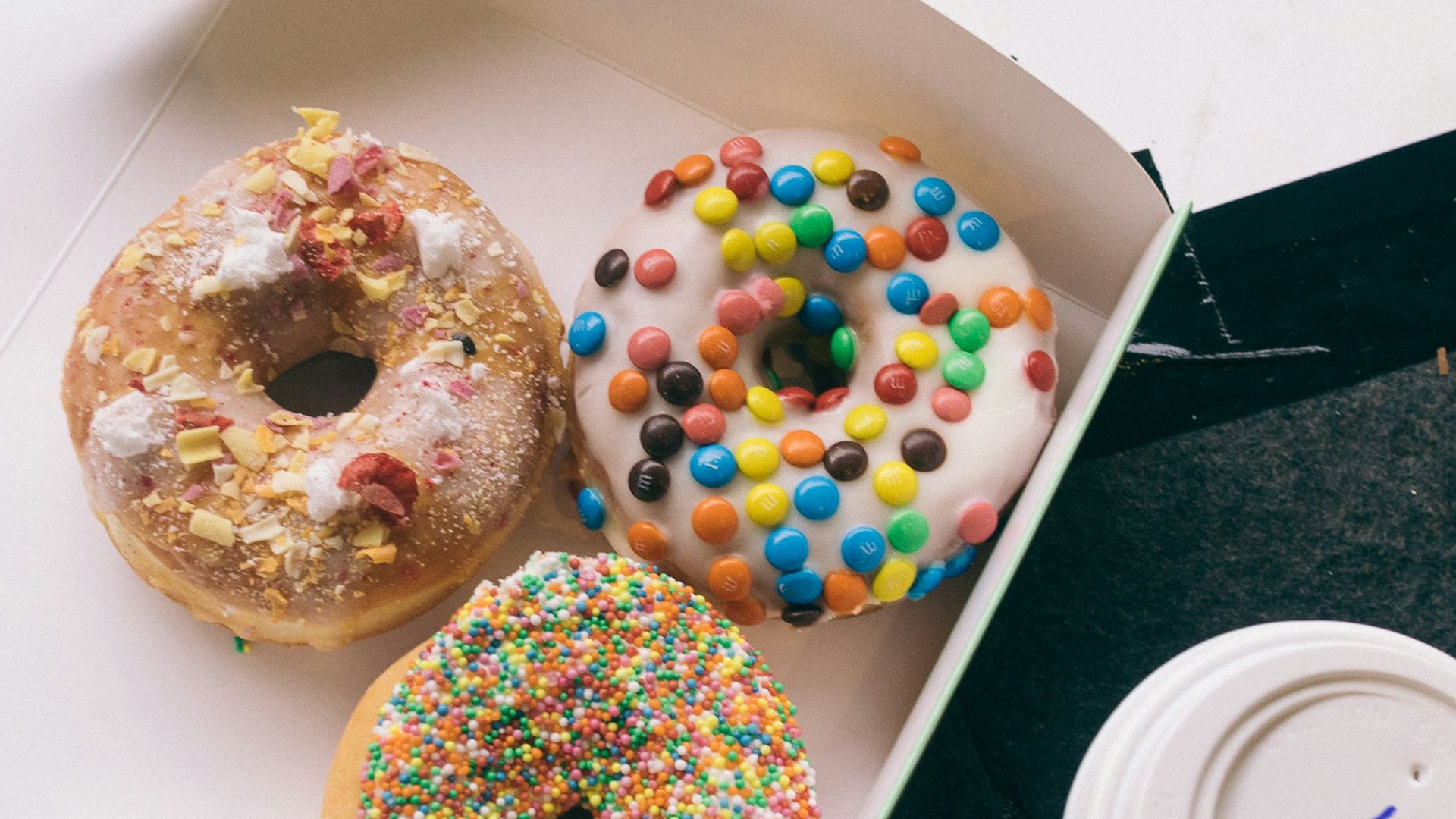 a box of three donuts with sprinkles and a cup of coffee
