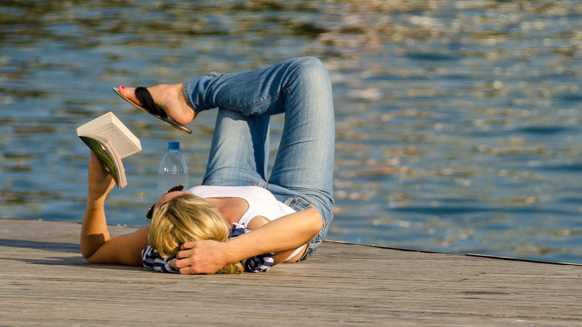woman in white tank top and gray pants lying on brown wooden dock during daytime
