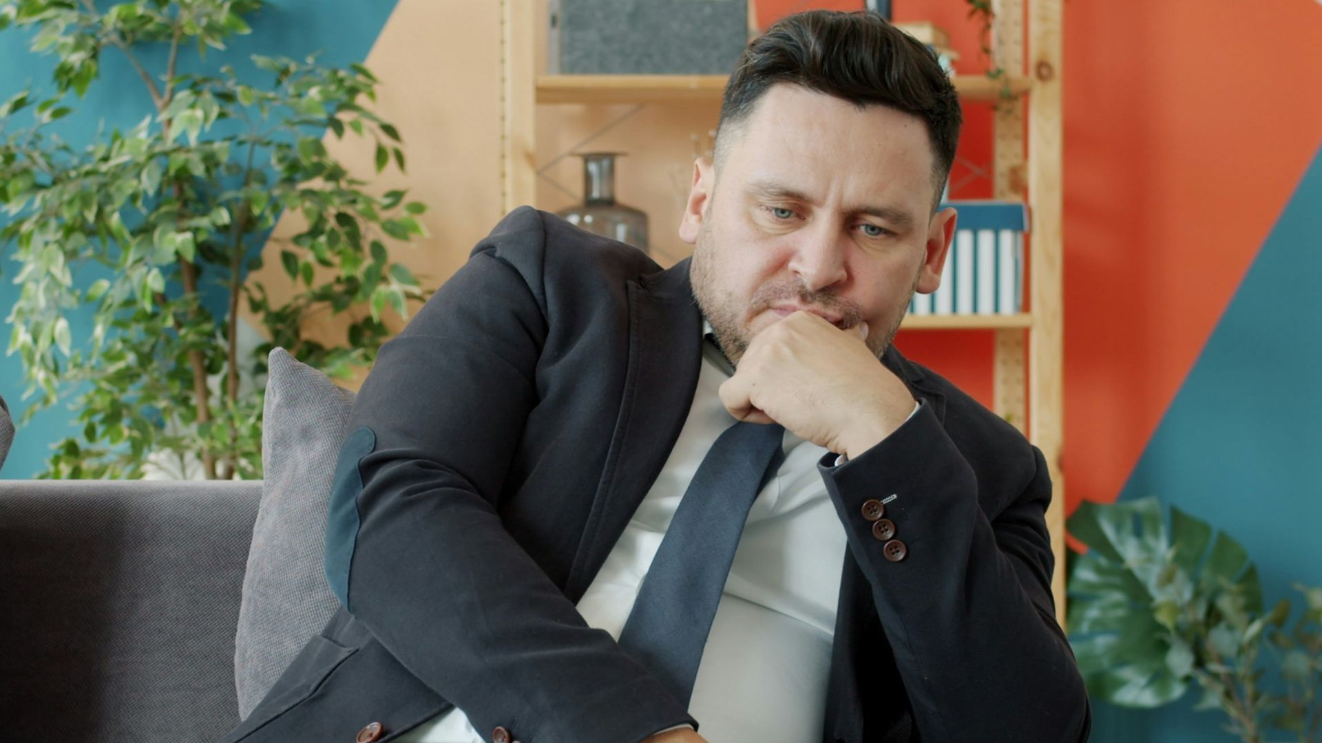 Man in suit sitting on couch looking thoughtful.