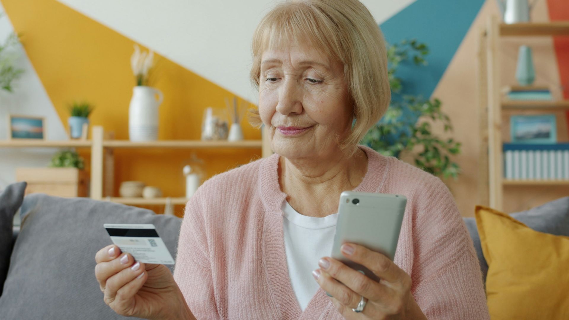 Elderly woman holding credit card and smartphone.
