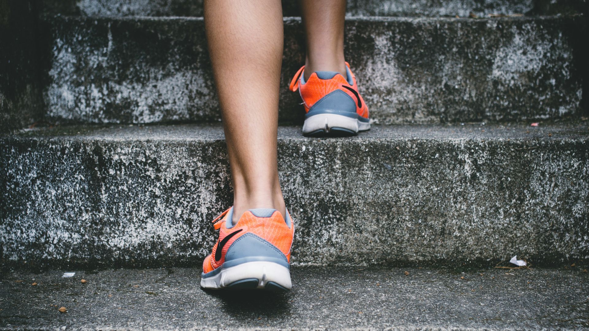 person wearing orange and gray Nike shoes walking on gray concrete stairs