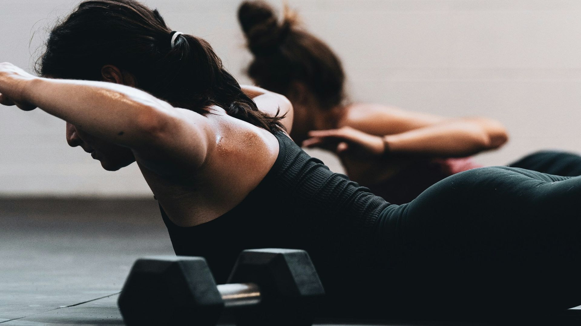 woman in black tank top and black leggings lying on black floor
