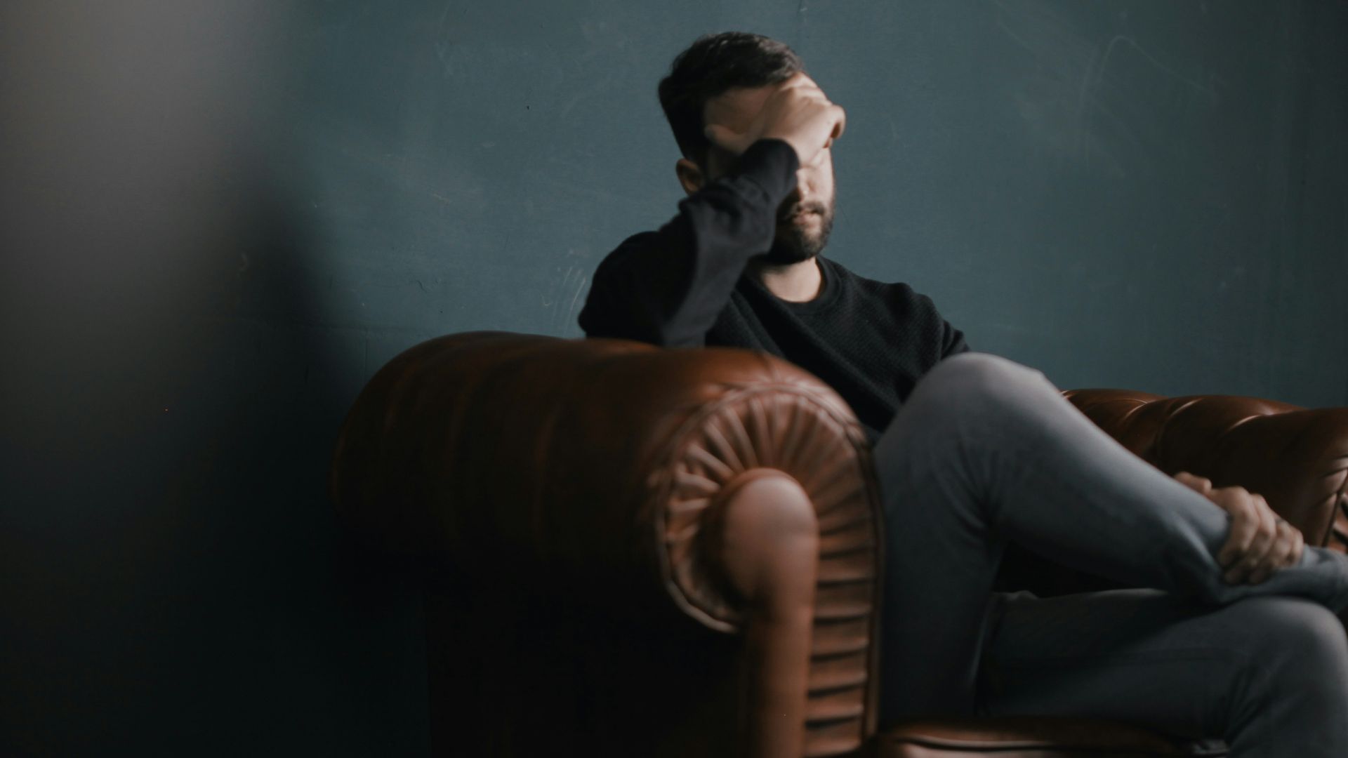 a man holds his head while sitting on a sofa