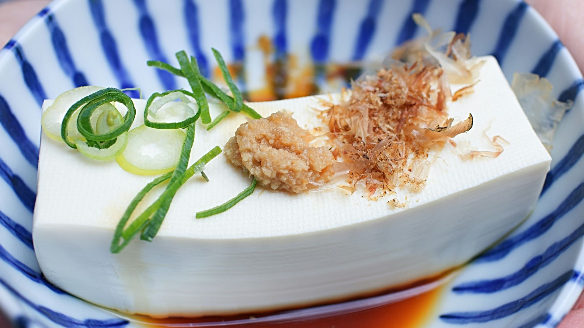 person holding white and blue ceramic plate with rice and sliced cucumber