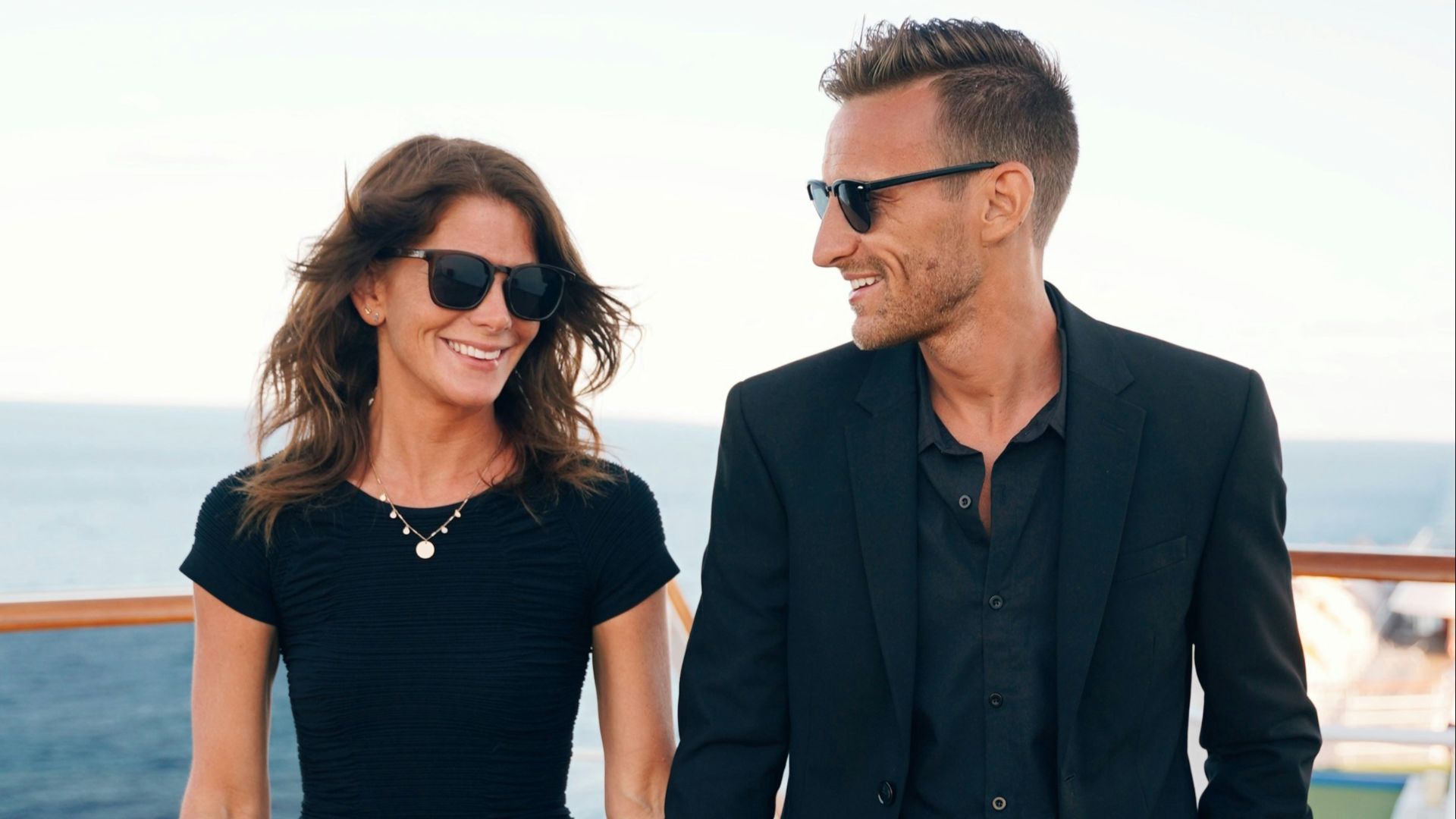 a man and woman wearing sunglasses and standing on a deck