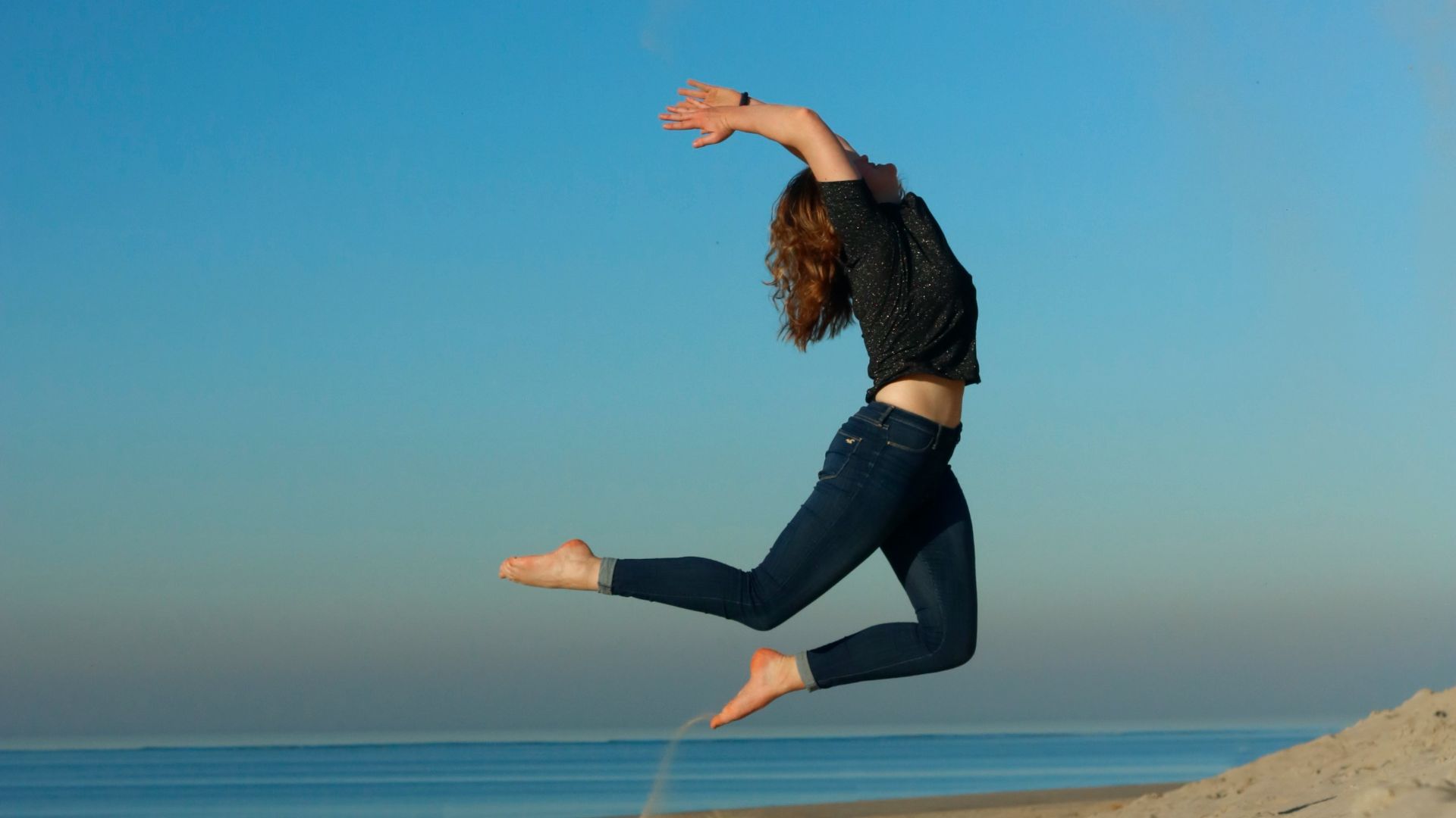 woman jumping on shore during daytime