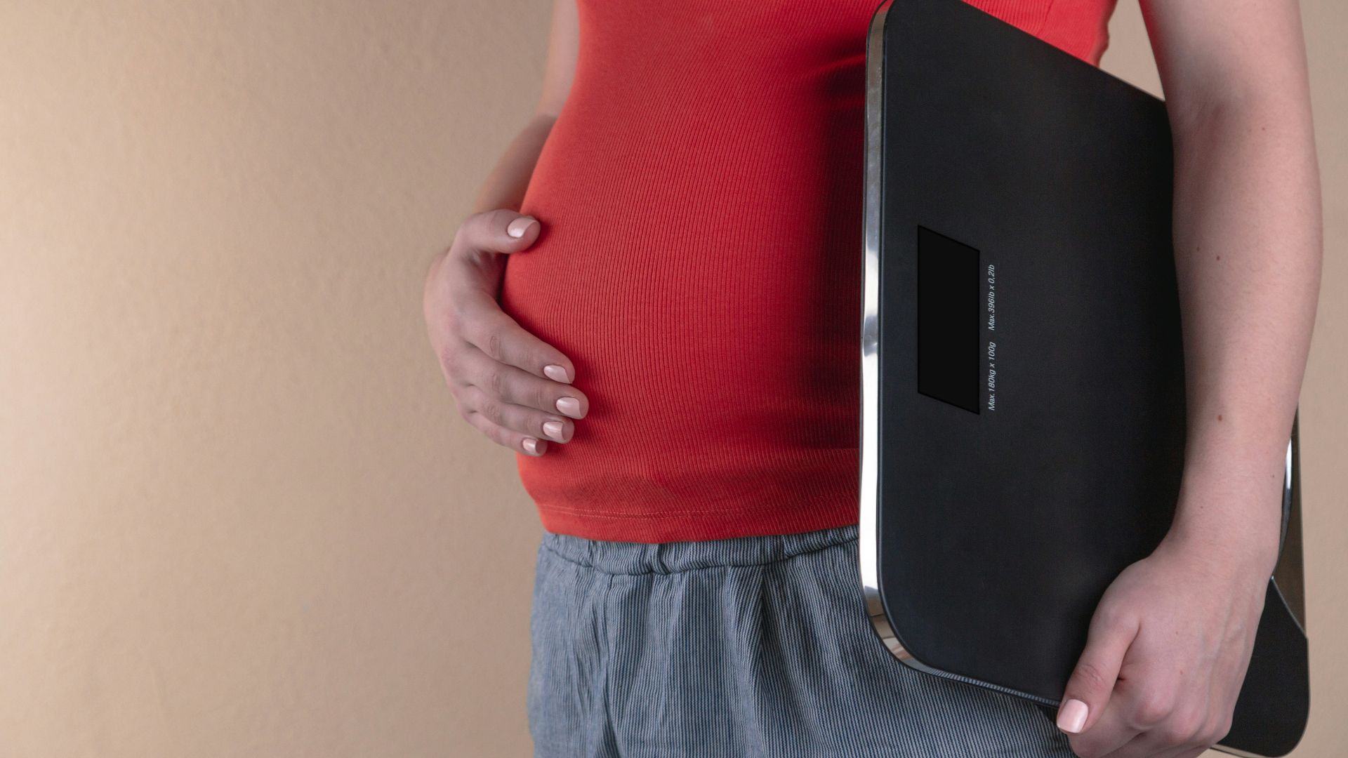 pregnant woman touching her belly and carrying a digital bathrooms cale