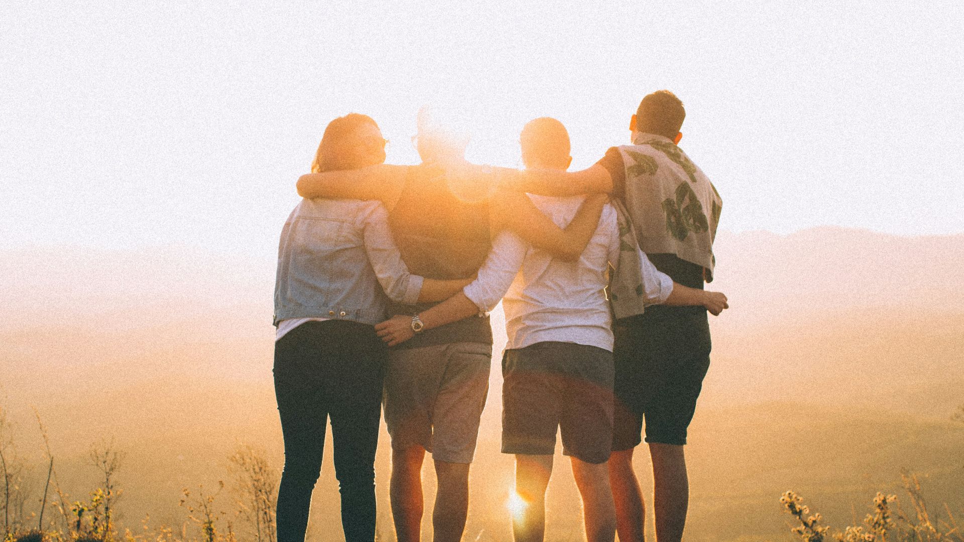 four person hands wrap around shoulders while looking at sunset