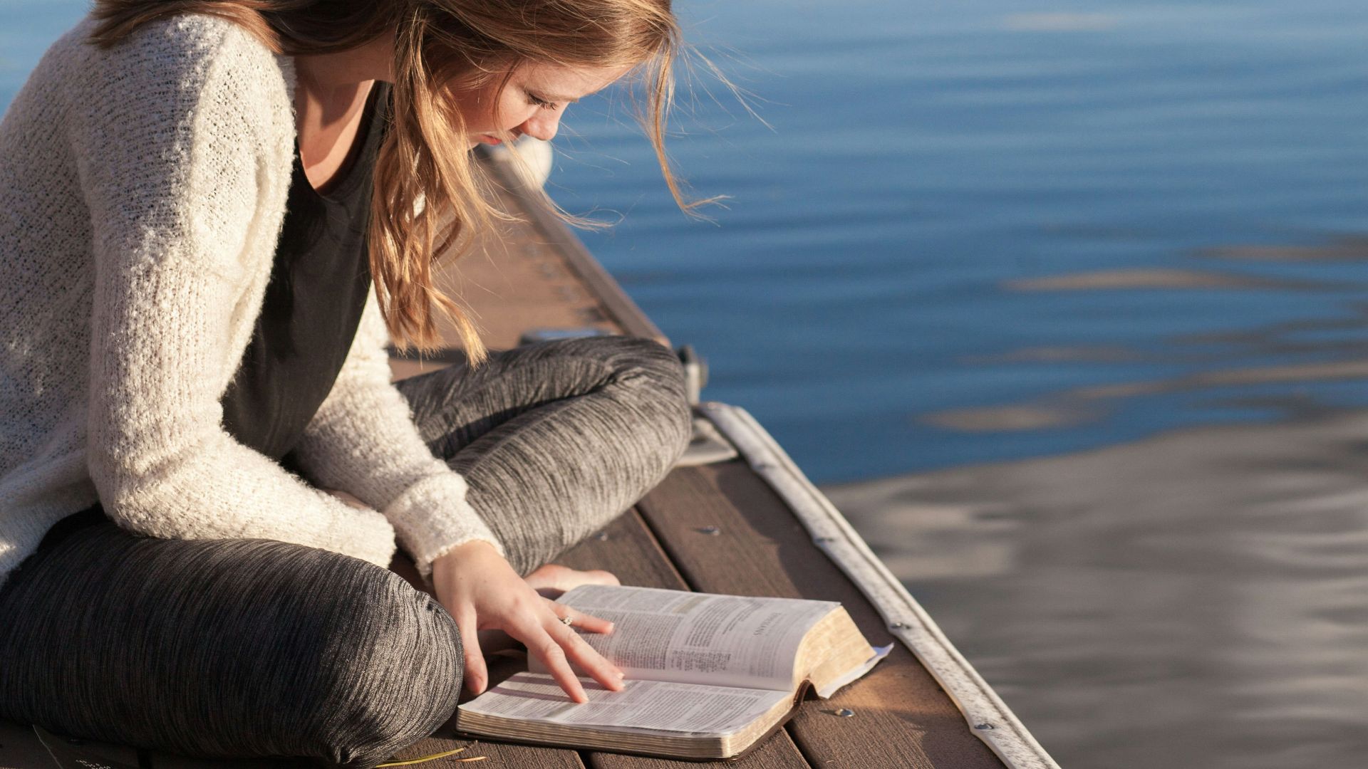 photo of woman reading book near body of water