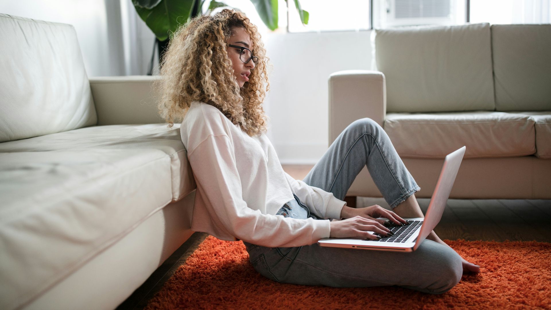 woman sitting on floor and leaning on couch using laptop