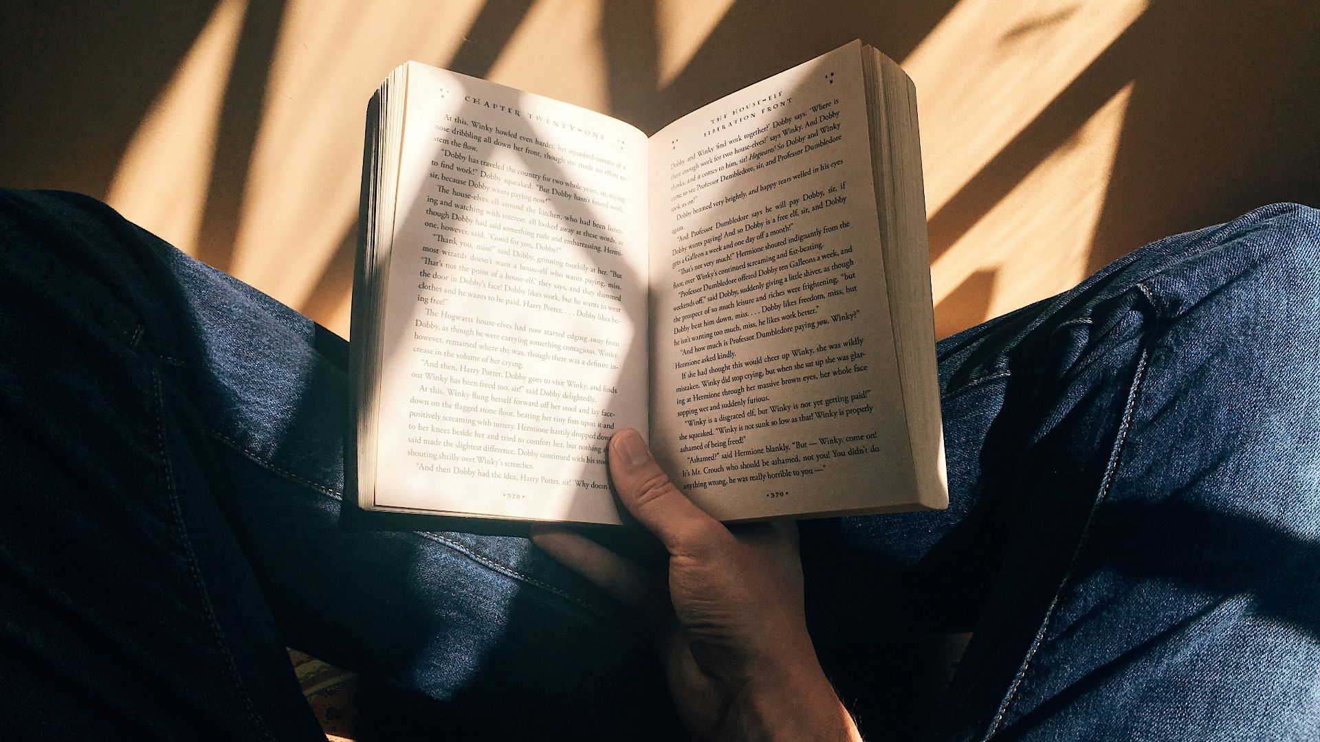 person holding book sitting on brown surface