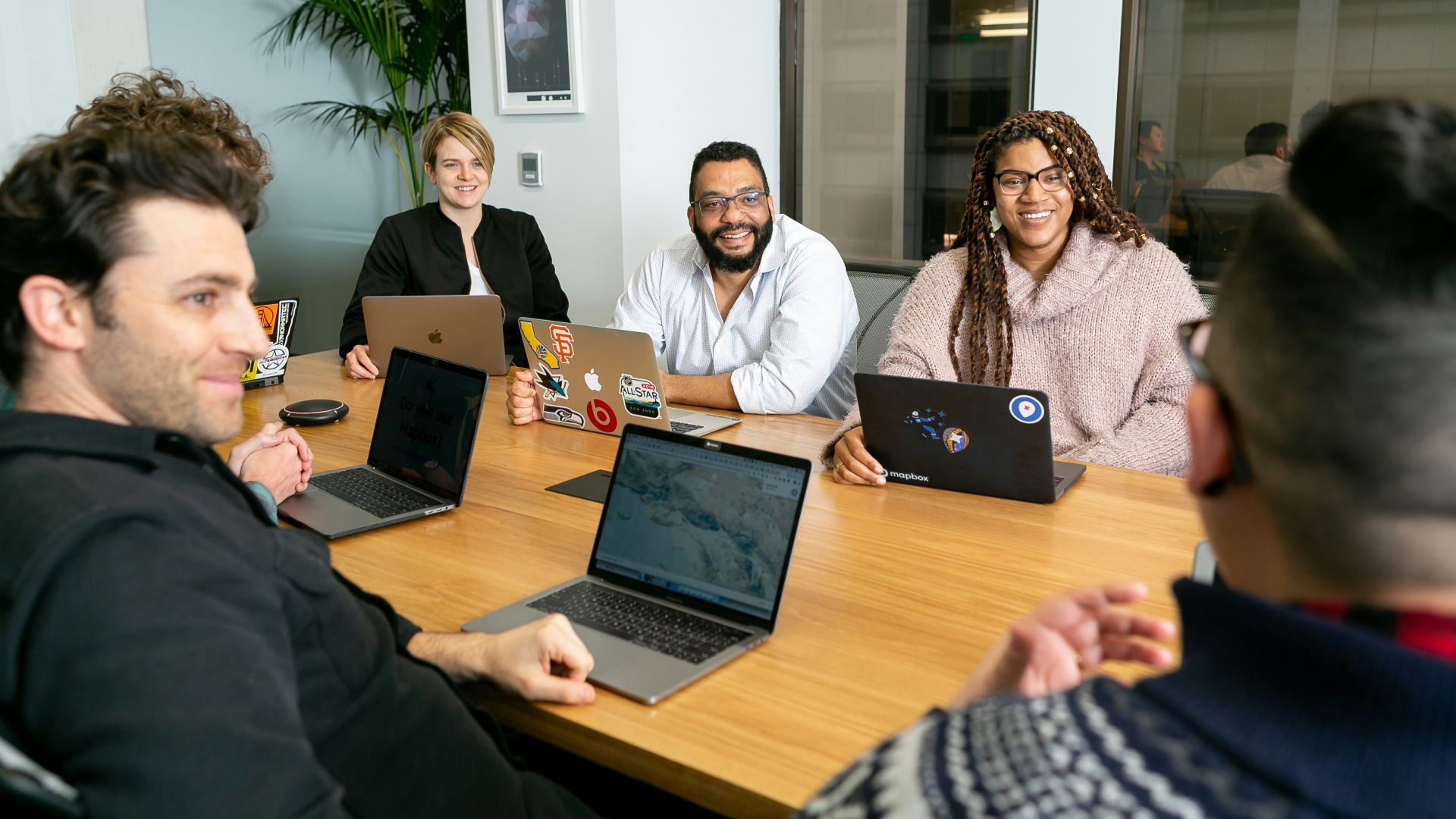 four people all on laptops, two men and two women, listen to person talking in a board meeting