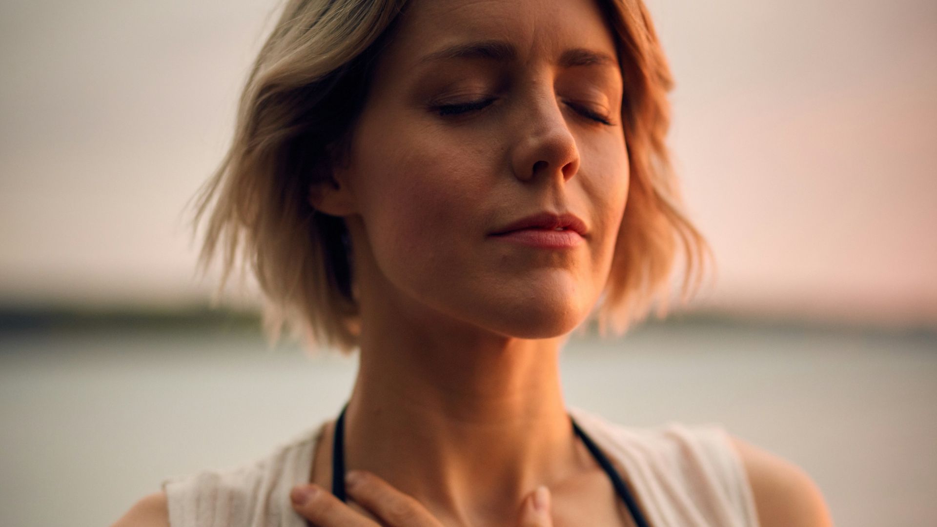 woman in white vest and black bikini with hand on chest