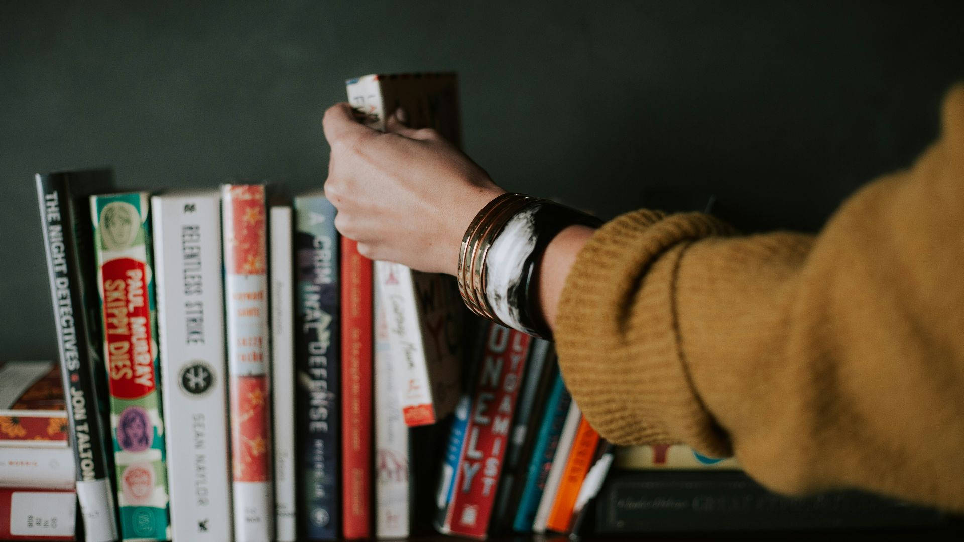 person picking white and red book on bookshelf