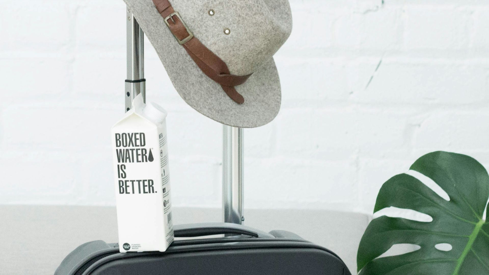 A hat and Boxed Water carton sit on a suitcase