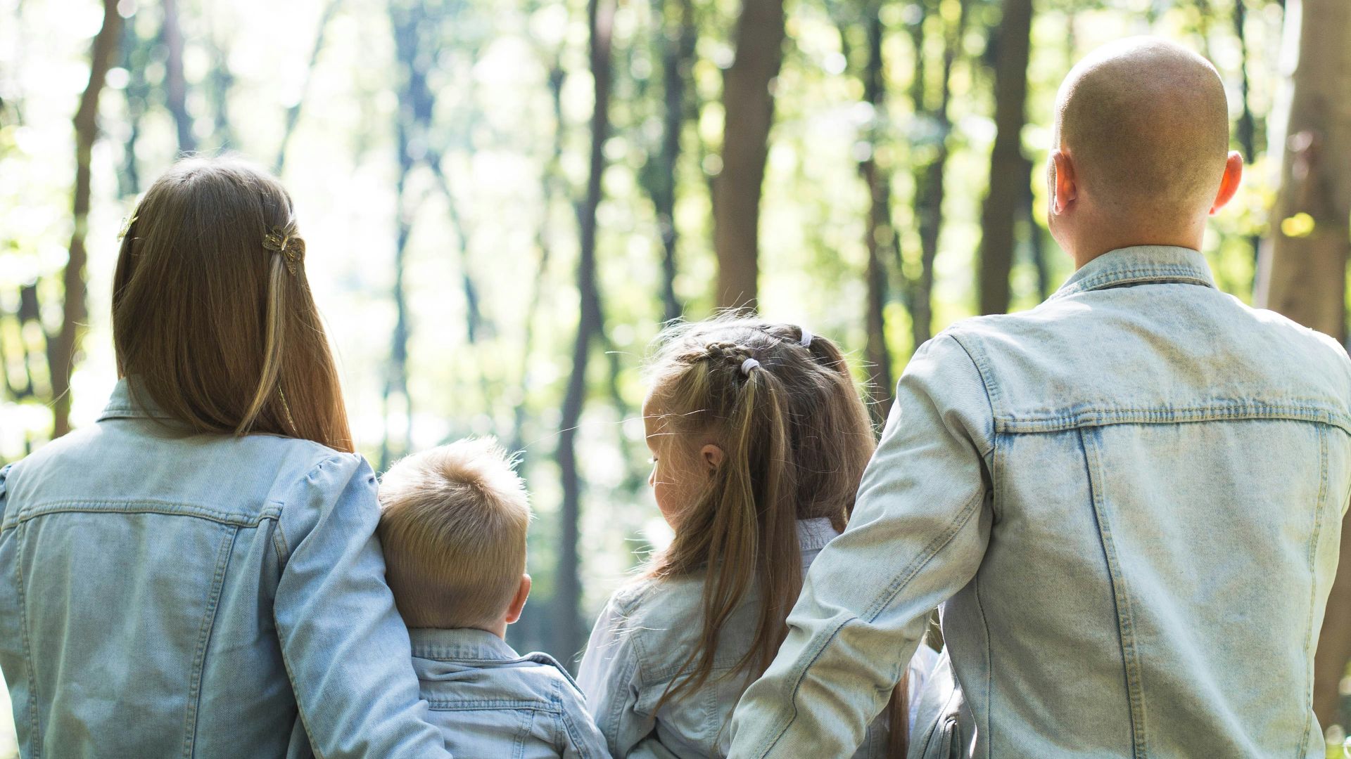 man and woman holding hands together with boy and girl looking at green trees during day
