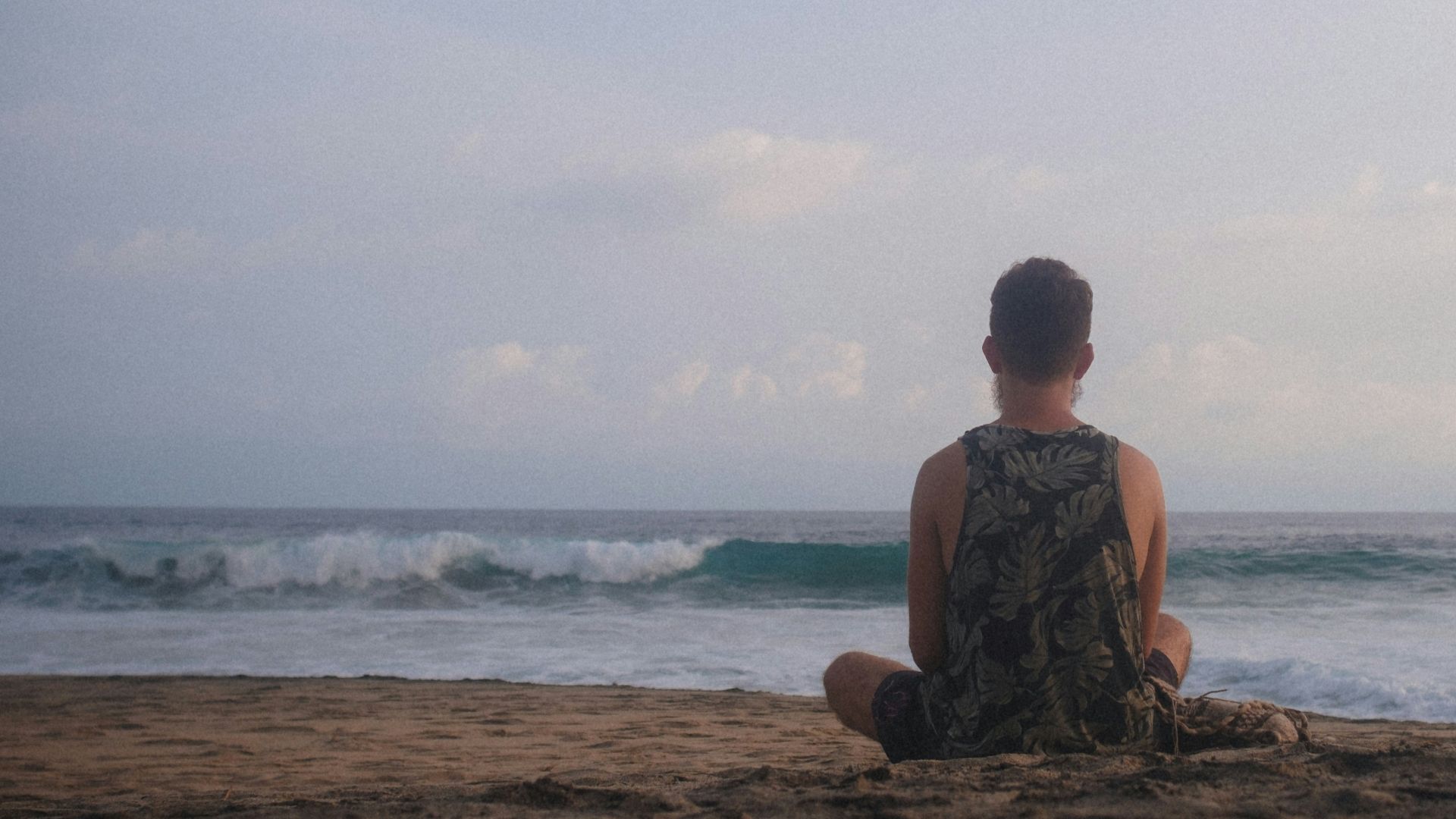 man in brown and black camouflage shirt sitting on brown rock near body of water during