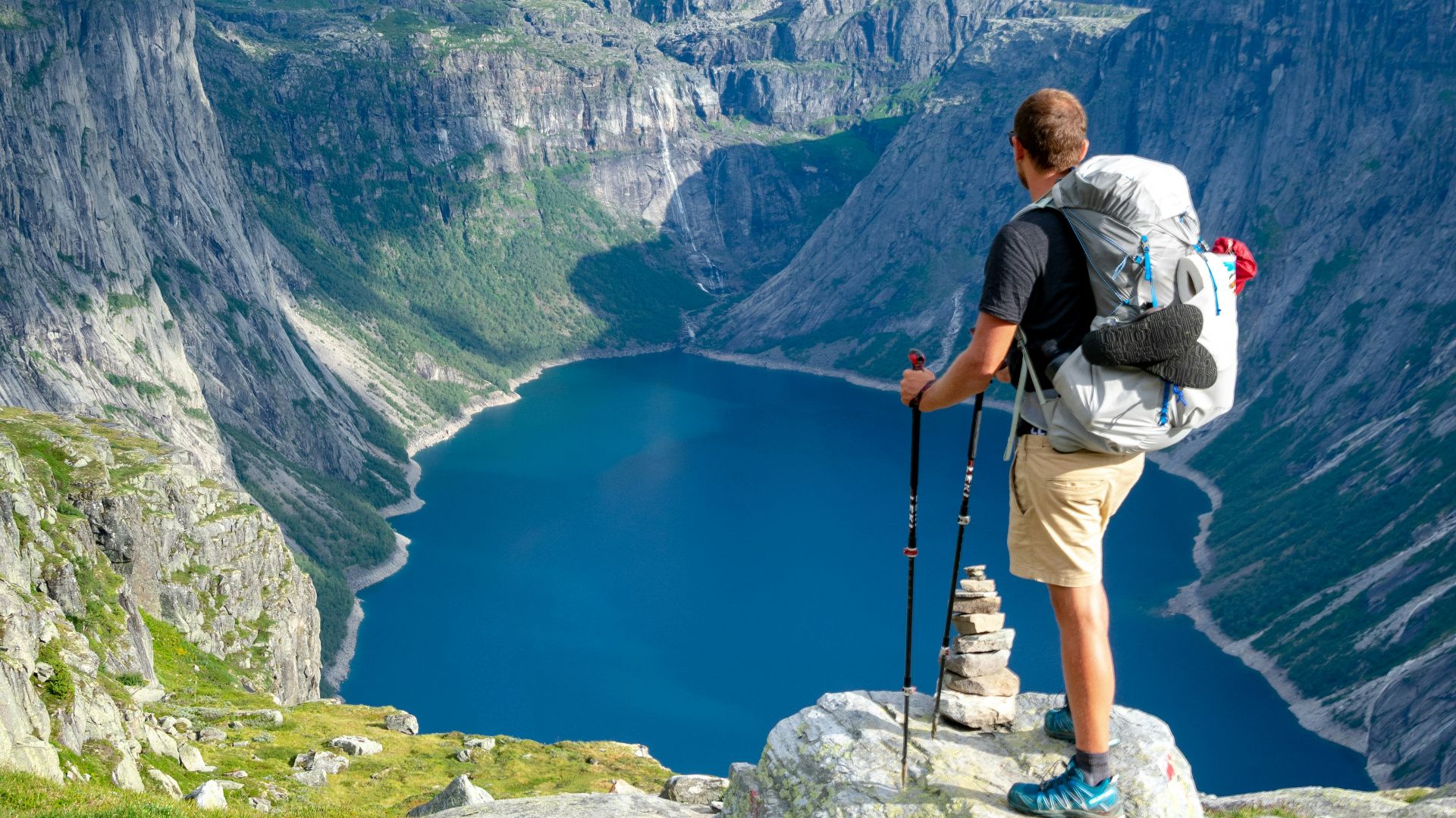 man standing on rock looking towards lake
