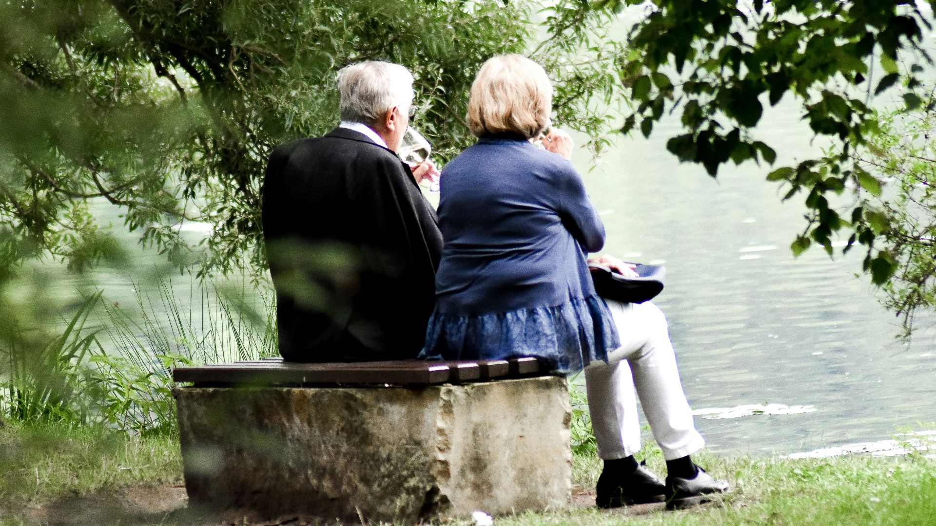 two people sitting on pavement facing on body of water