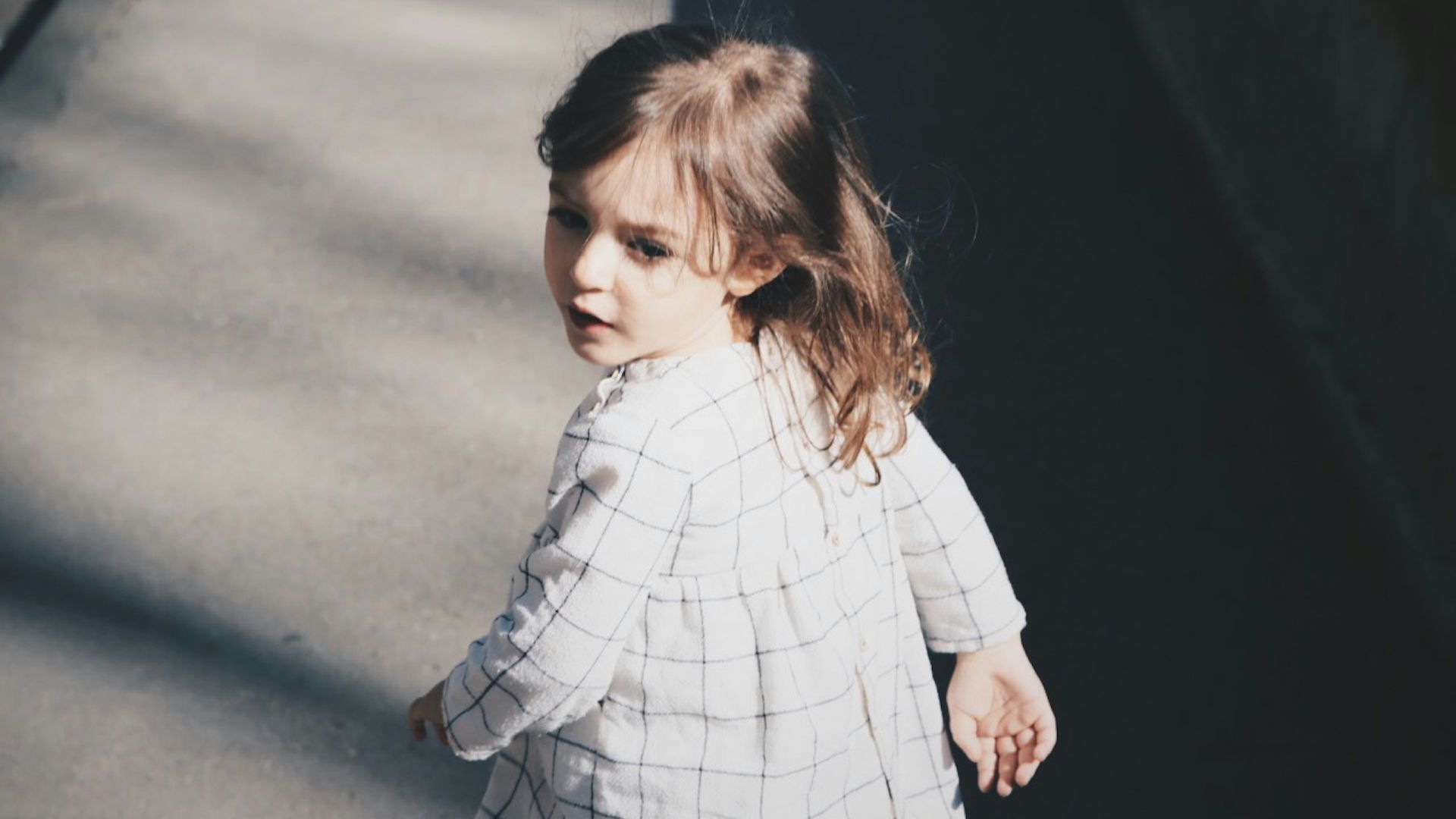 toddler girl walking on gray concrete road at daytime
