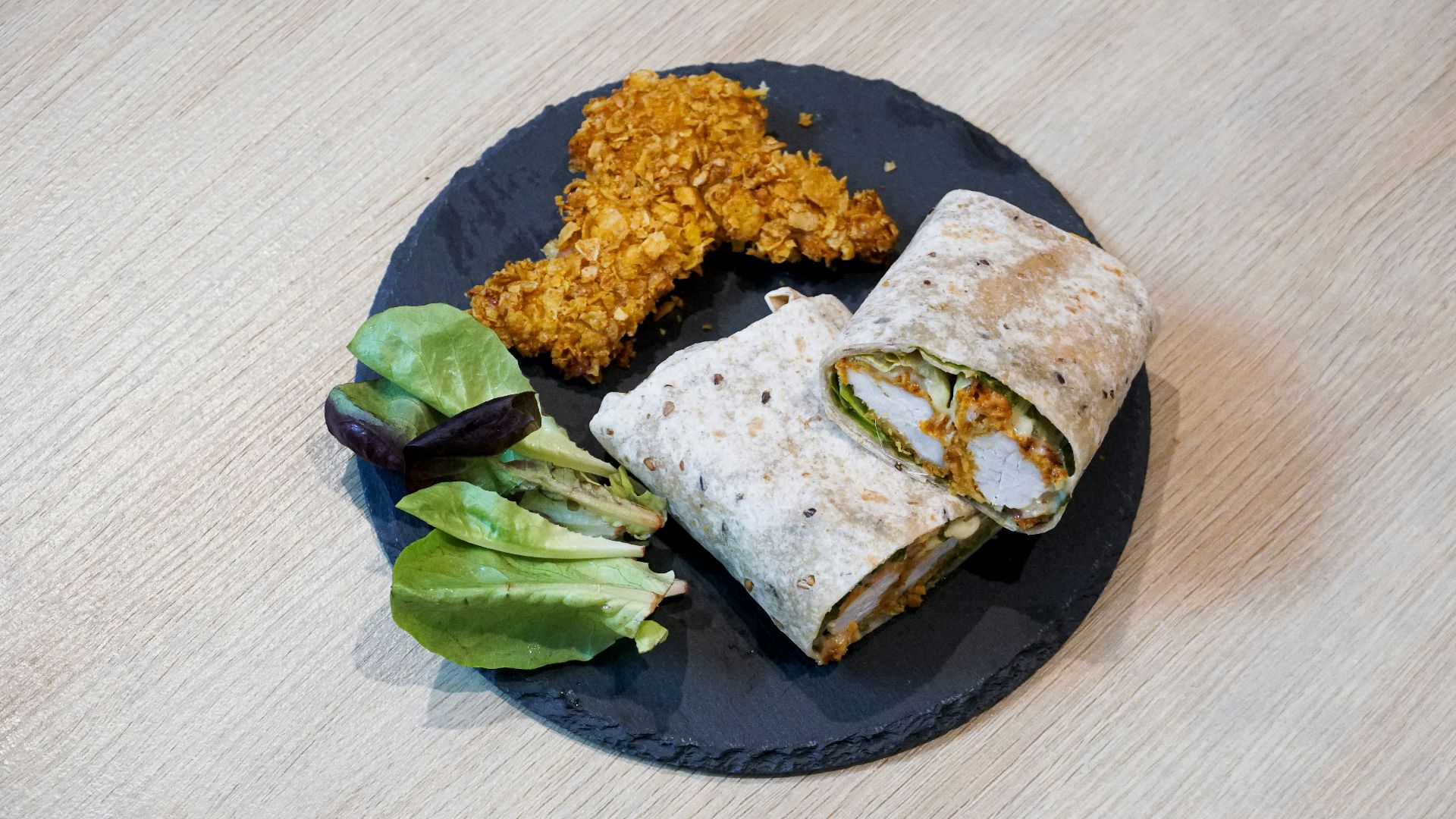 a black plate topped with a burrito and a salad