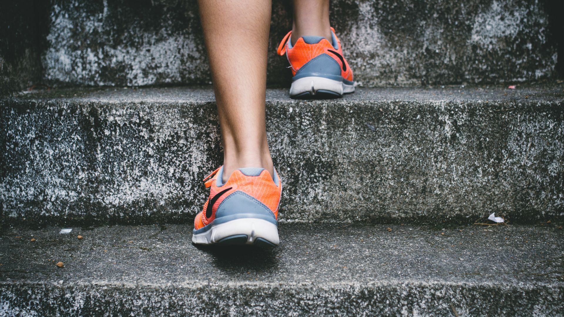 person wearing orange and gray Nike shoes walking on gray concrete stairs