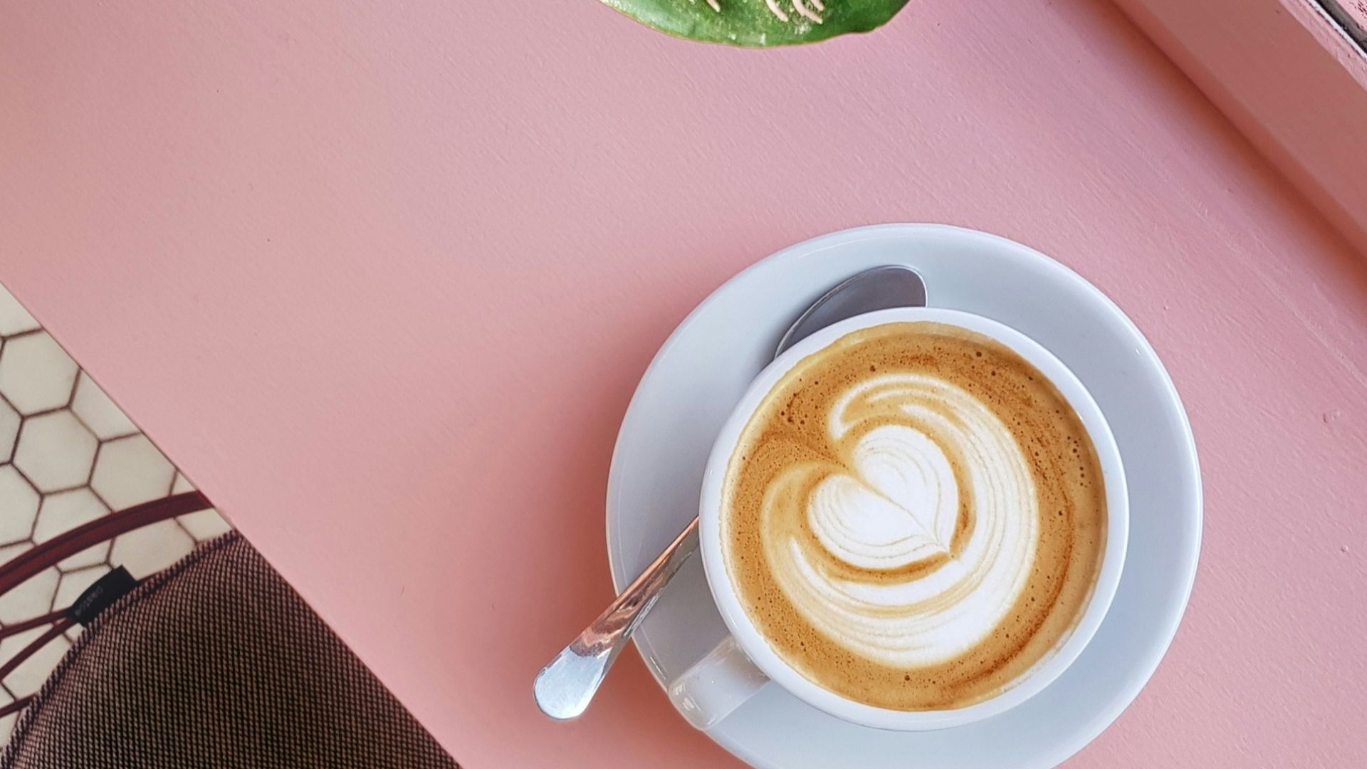 cup of coffee on saucer with teaspoon on pink tabletop