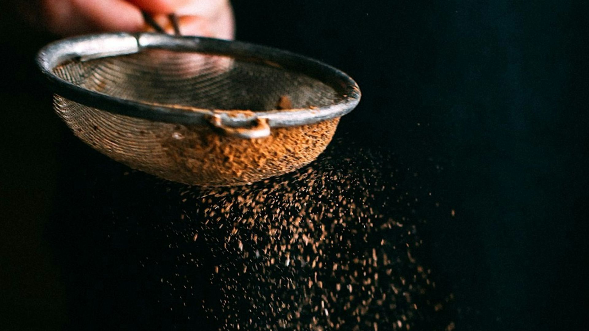 person pouring chocolate powder on cake