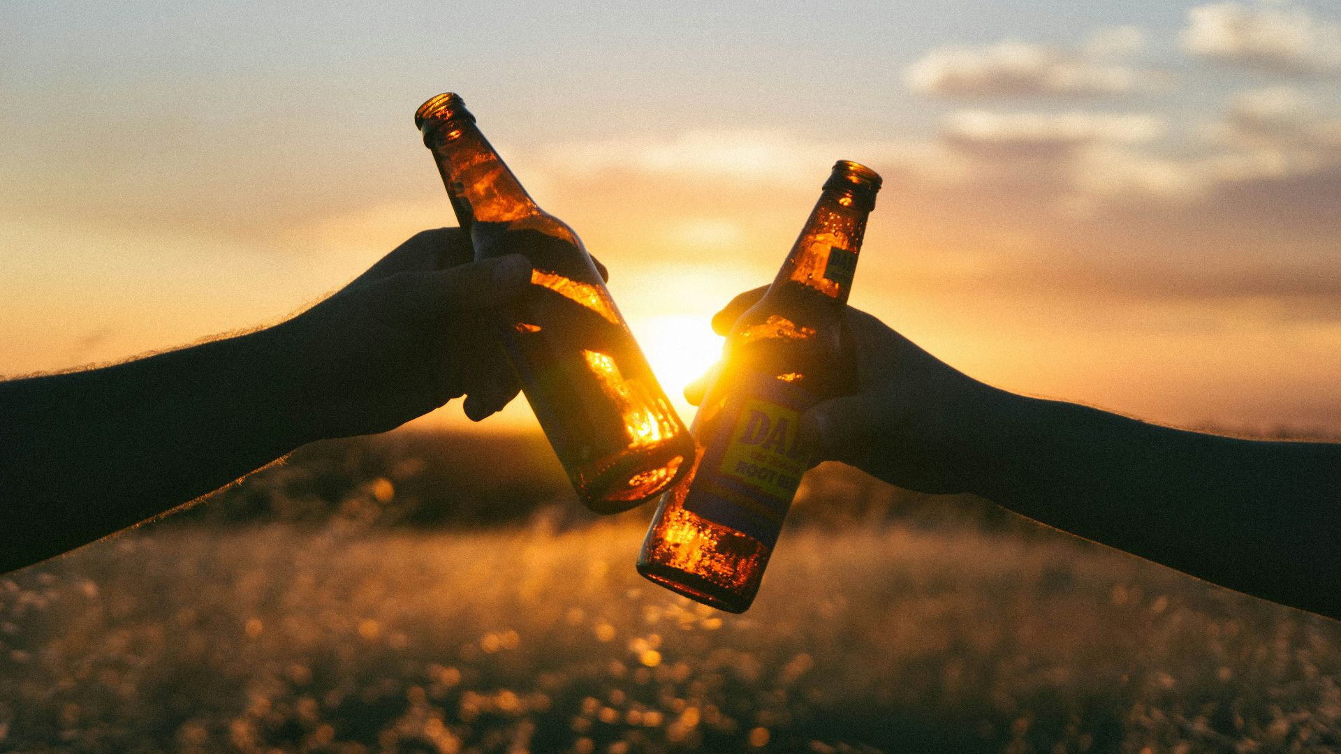 photography of person holding glass bottles during sunset