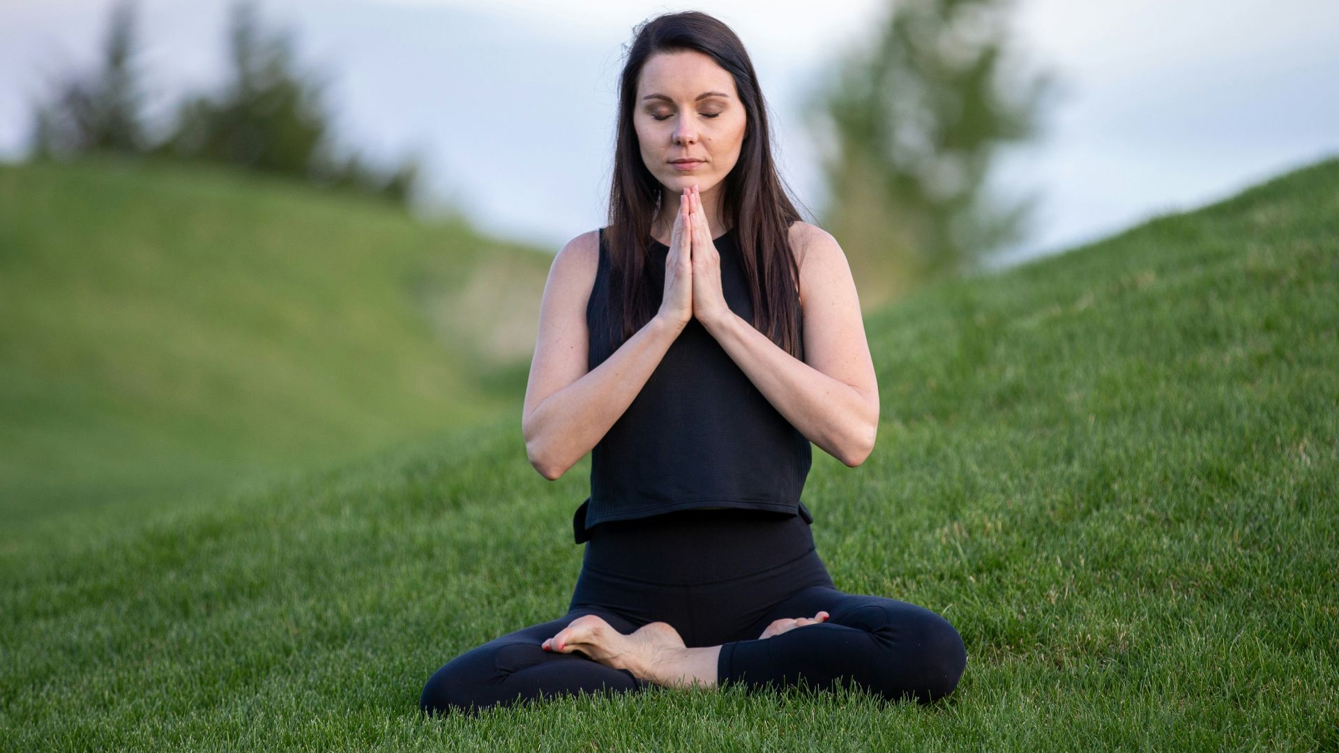woman in black tank top and black pants sitting on green grass field during daytime