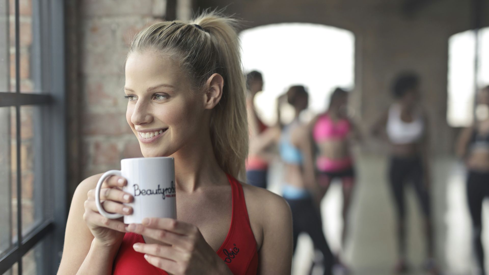 woman holding white ceramic mug while smiling near glass window