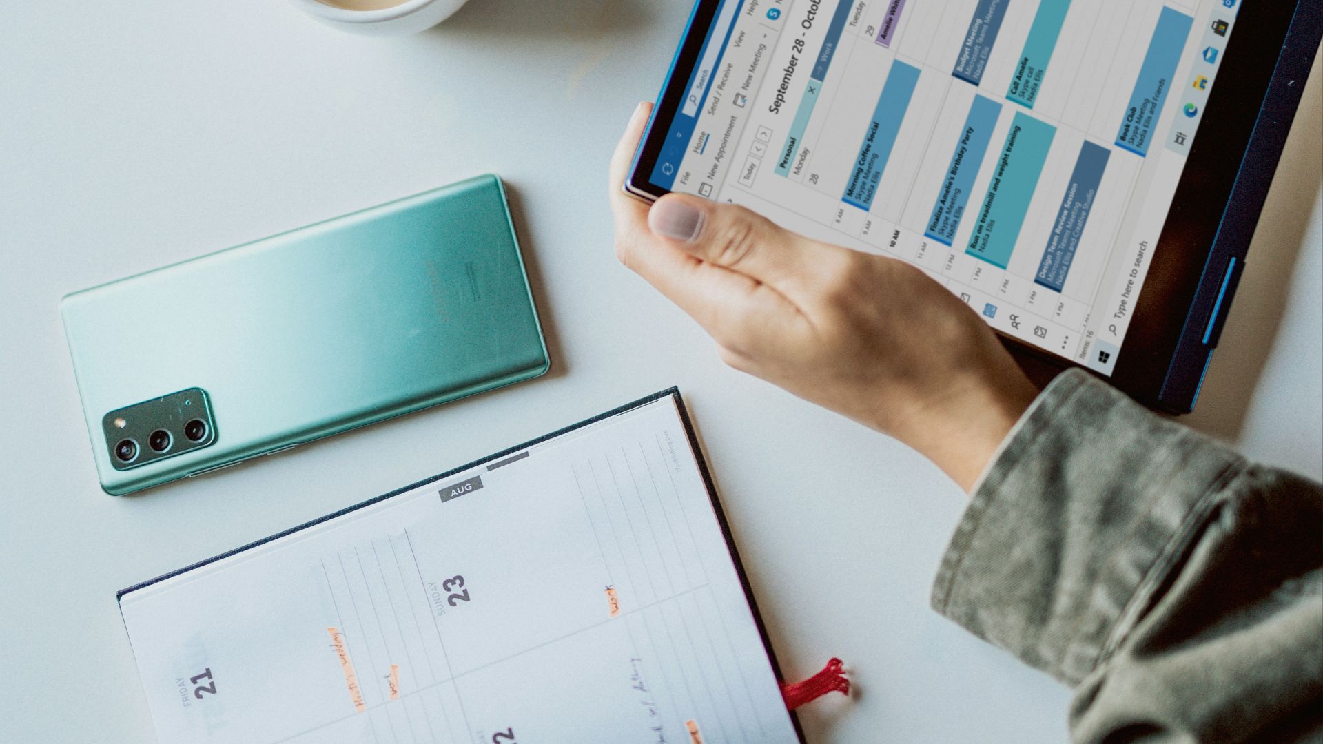 person holding ipad near white ceramic mug and laptop