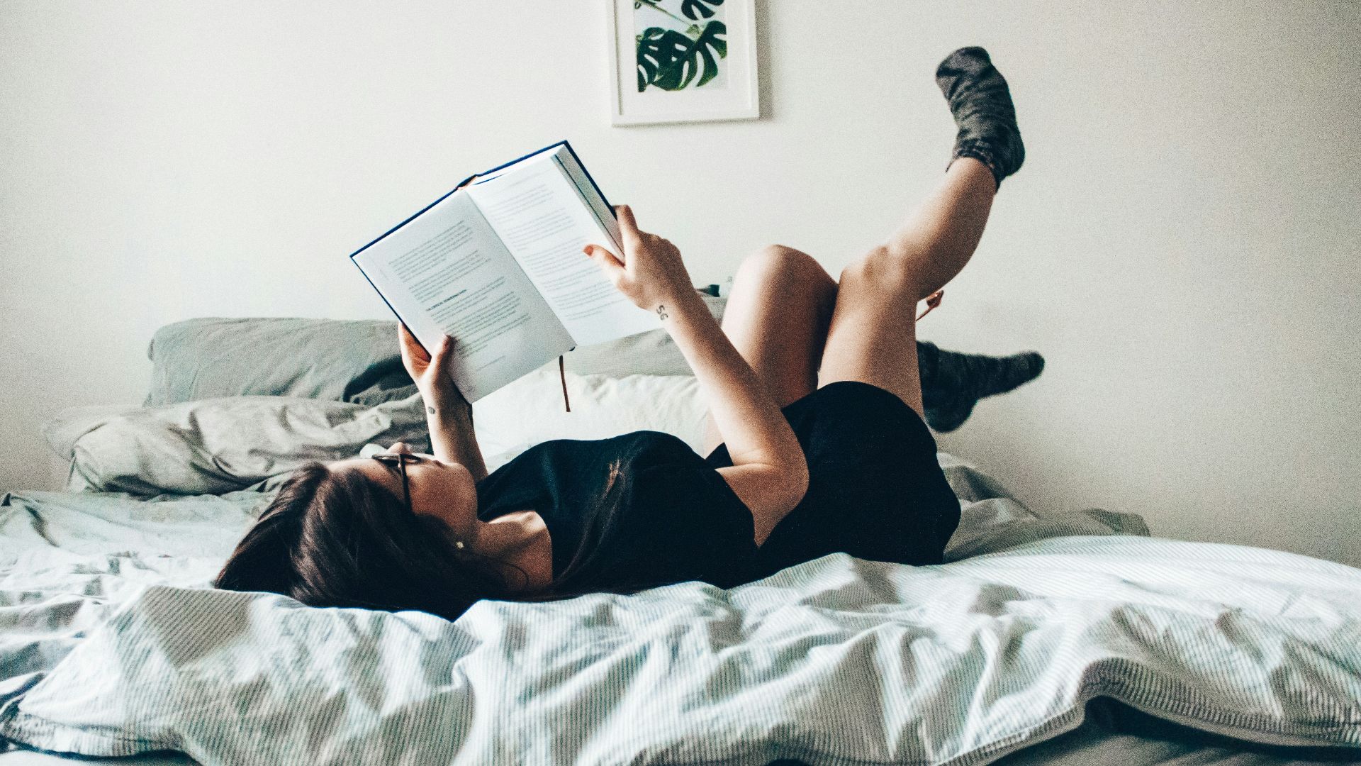 woman in black dress lying on bed while reading book