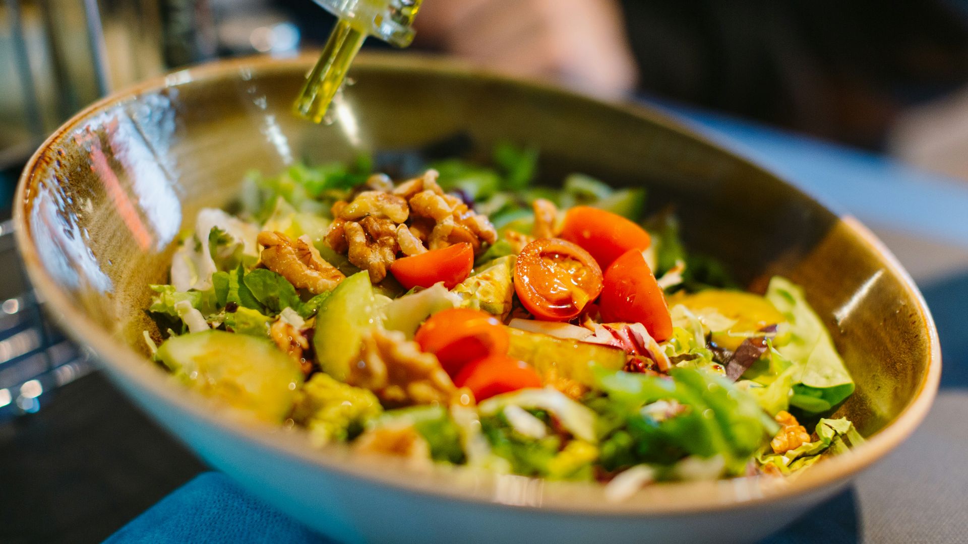 a salad in a bowl with dressing being drizzled over it