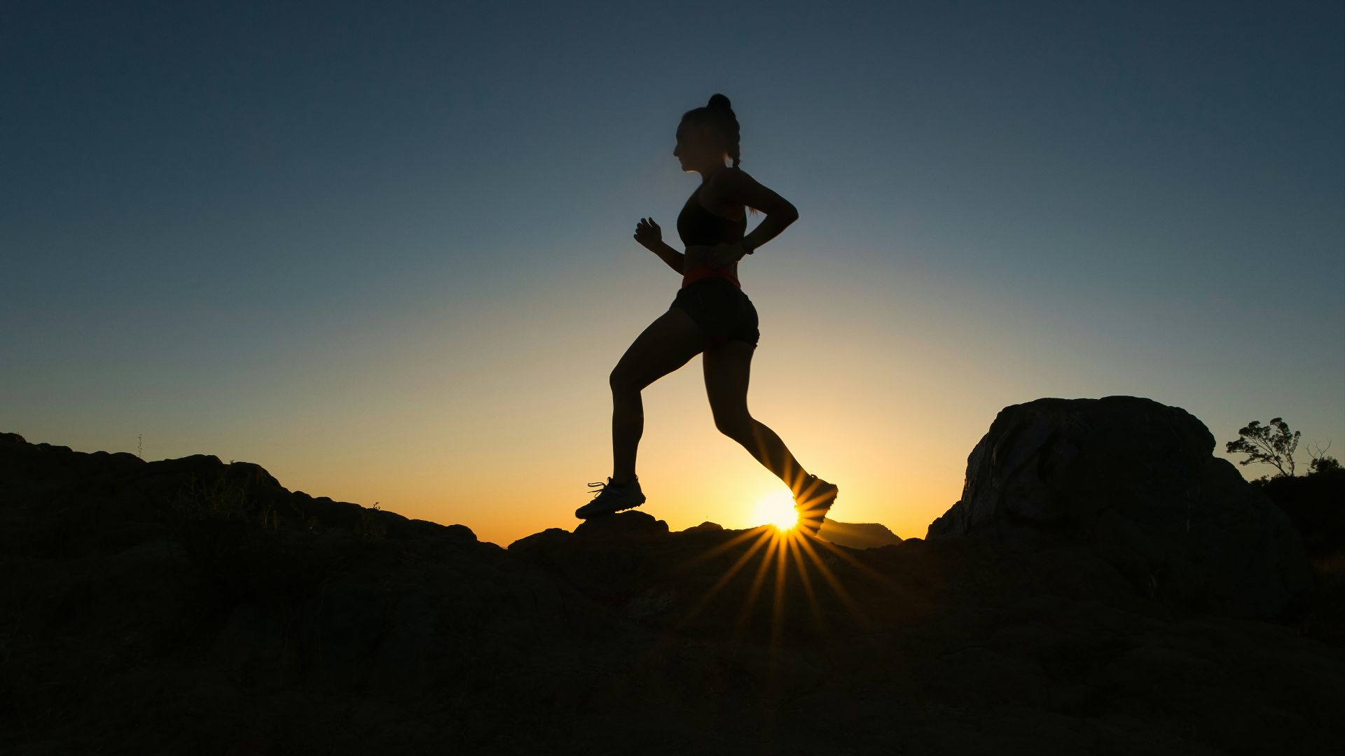 silhouette of man jumping on rocky mountain during sunset