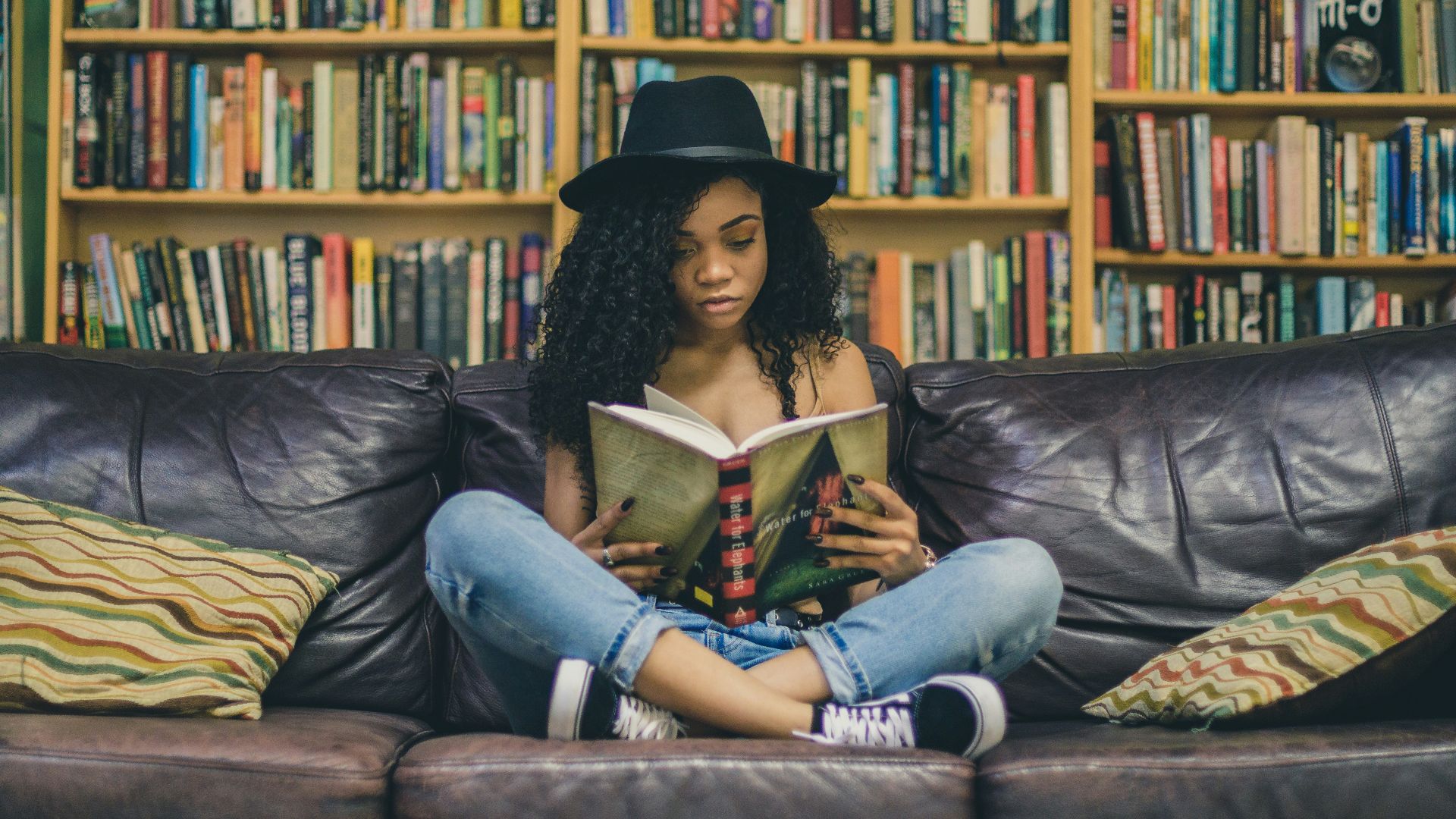 woman reading a book while sitting on black leather 3-seat couch