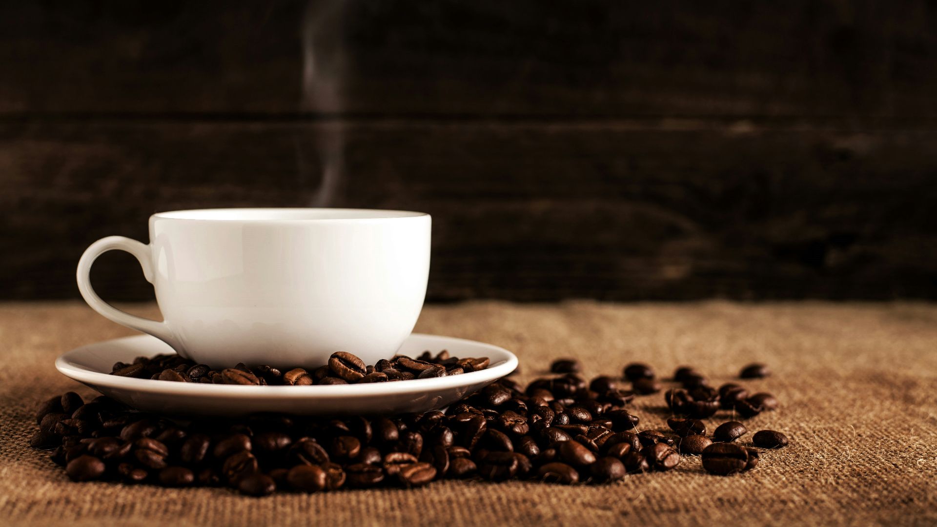 white ceramic mug and saucer with coffee beans on brown textile