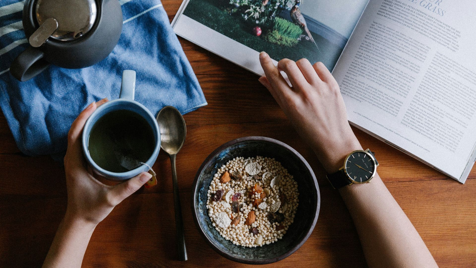 person holding blue ceramic mug and white magazine