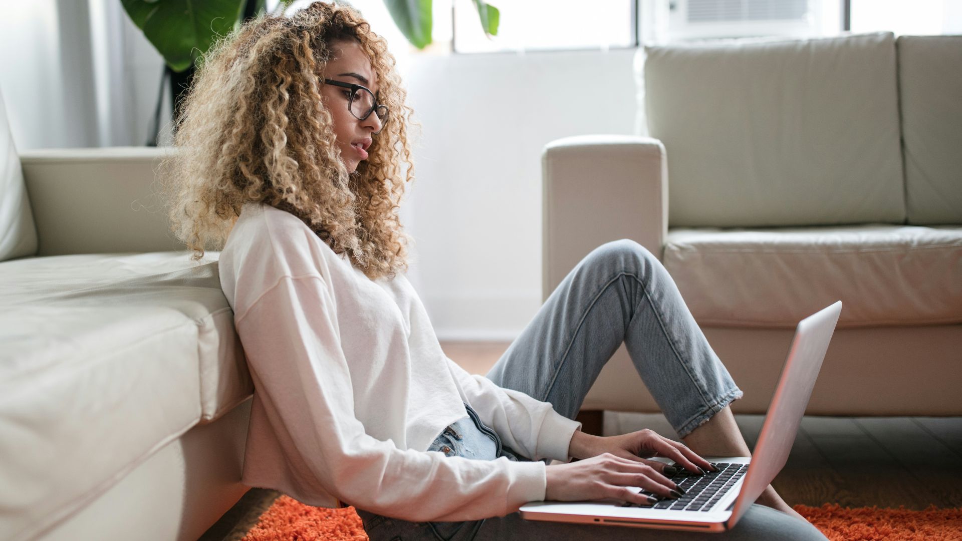 woman sitting on floor and leaning on couch using laptop