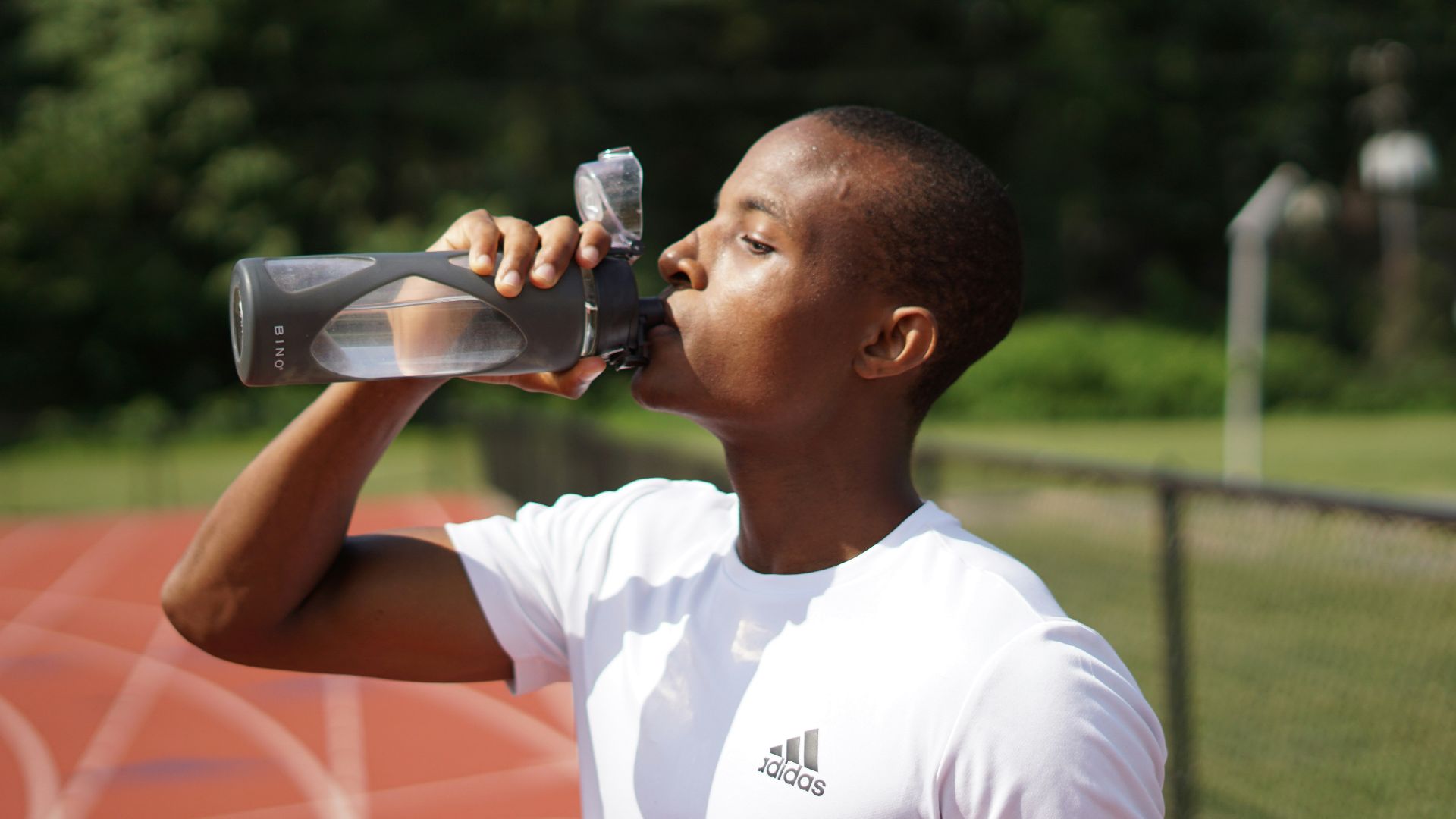 man in white crew neck t-shirt drinking from black sports bottle