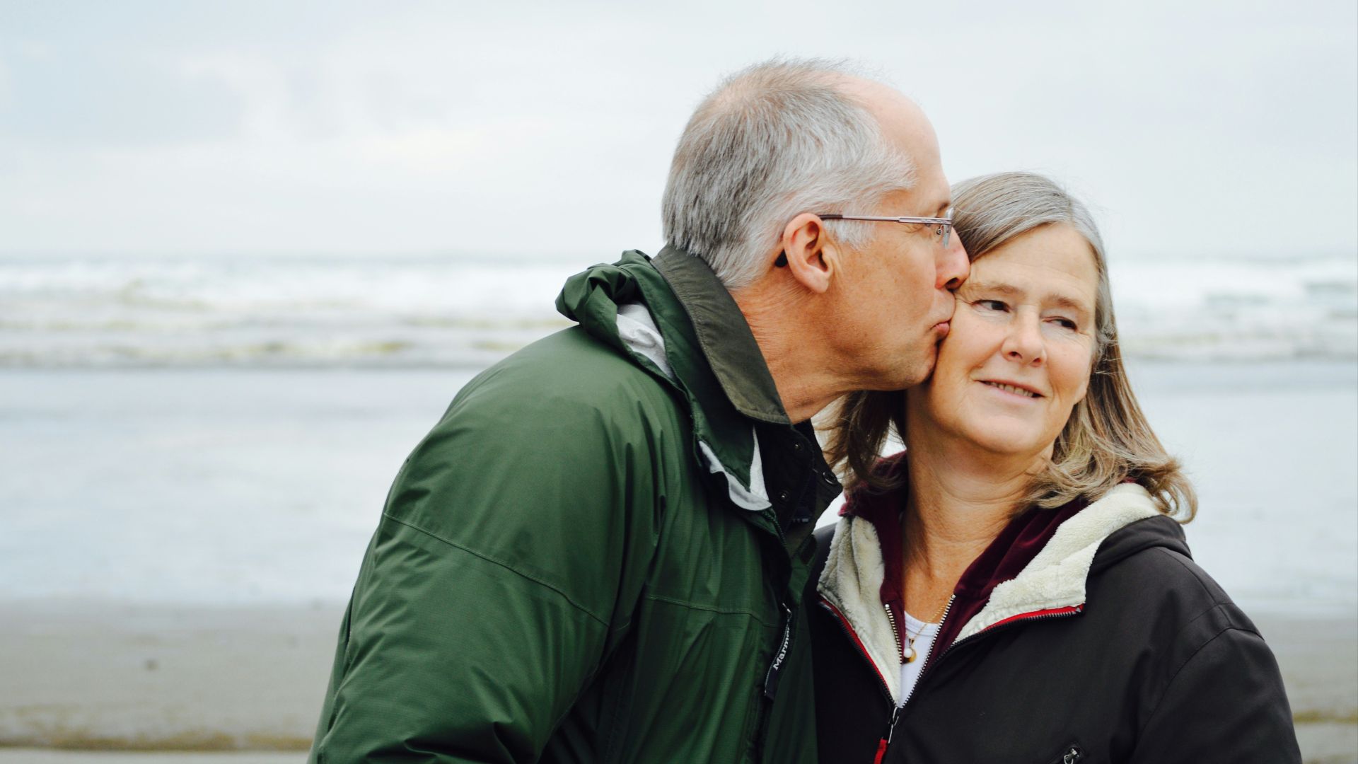 man kissing woman on check beside body of water