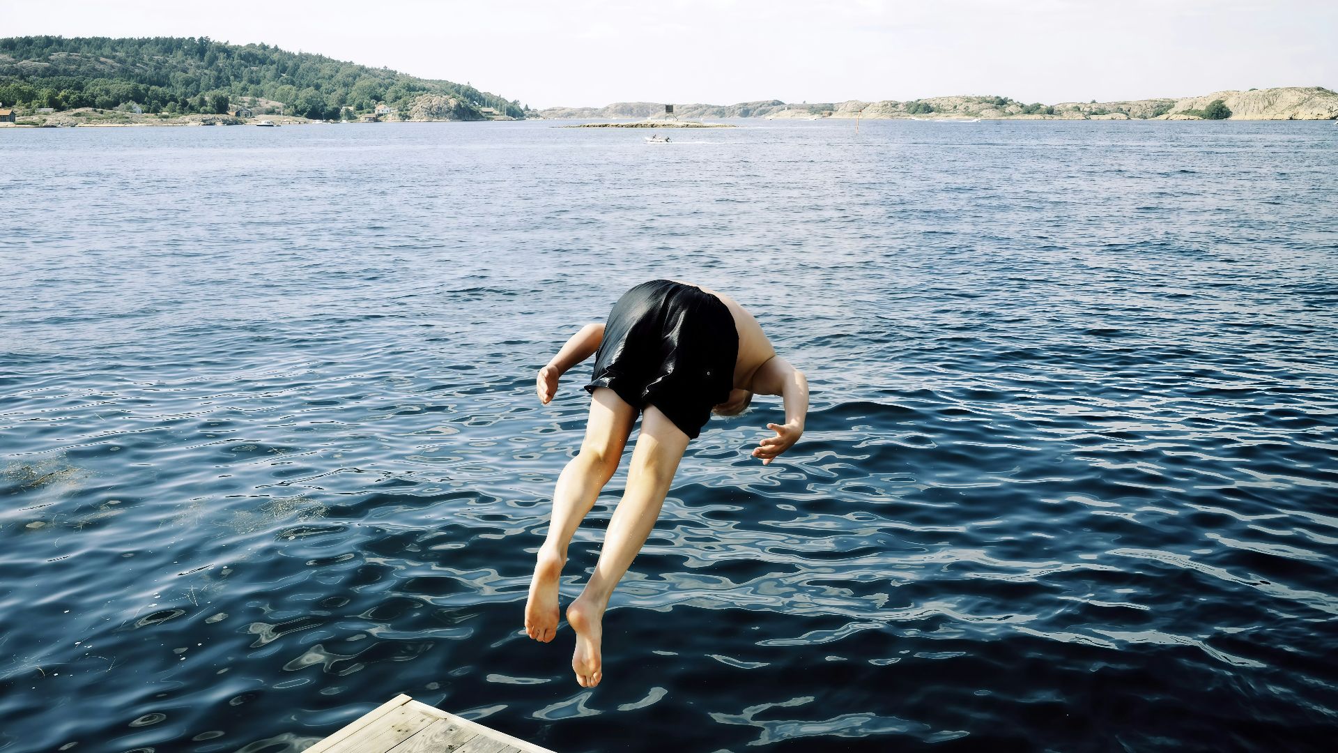 Person diving into the blue ocean from a wooden dock.