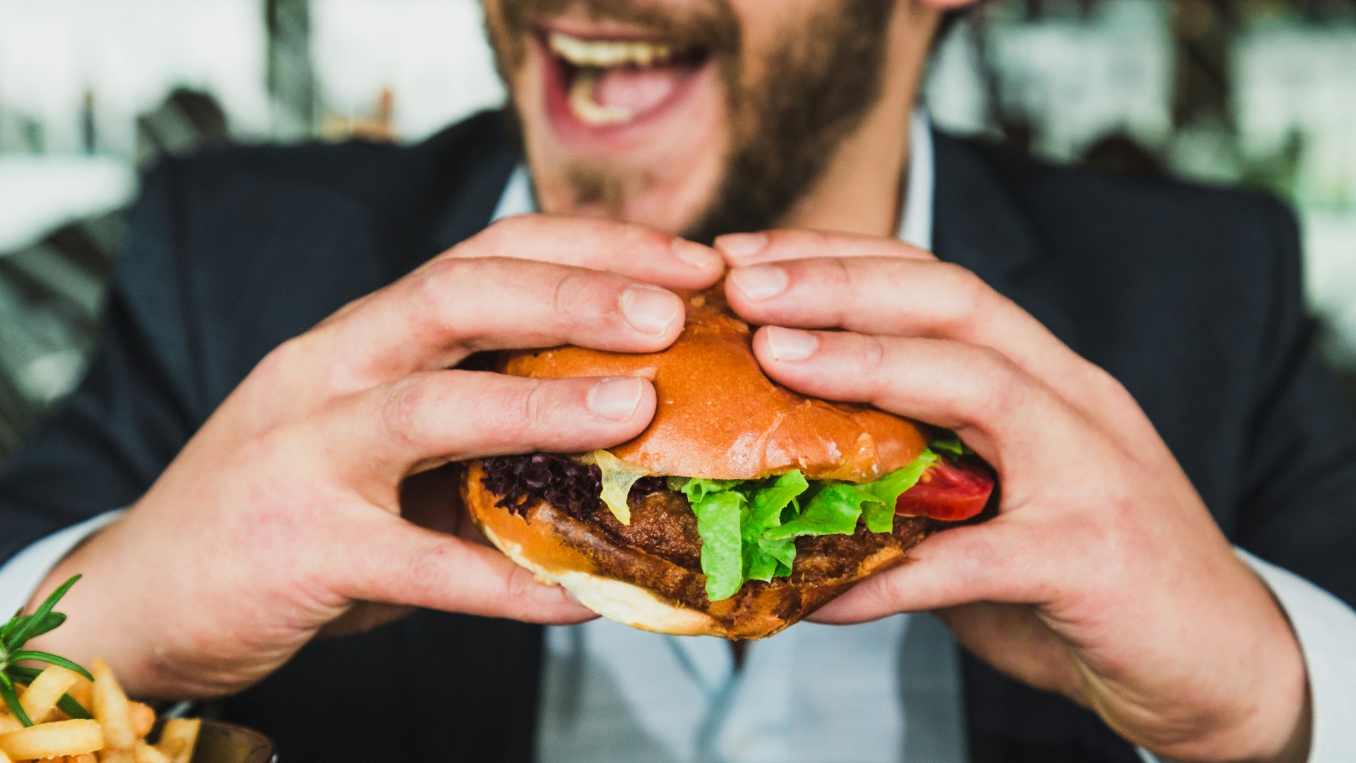 person holding burger bun with vegetables and meat