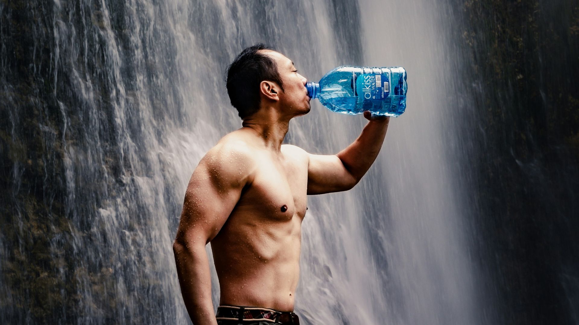man drinking water beside waterfalals