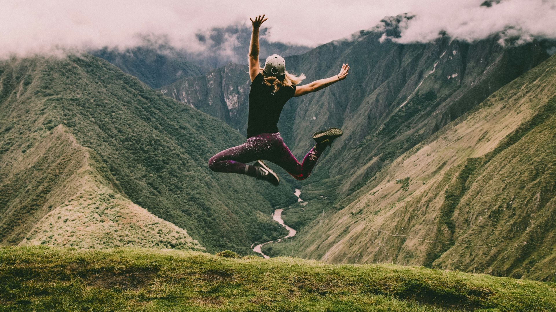 woman jumping on green mountains