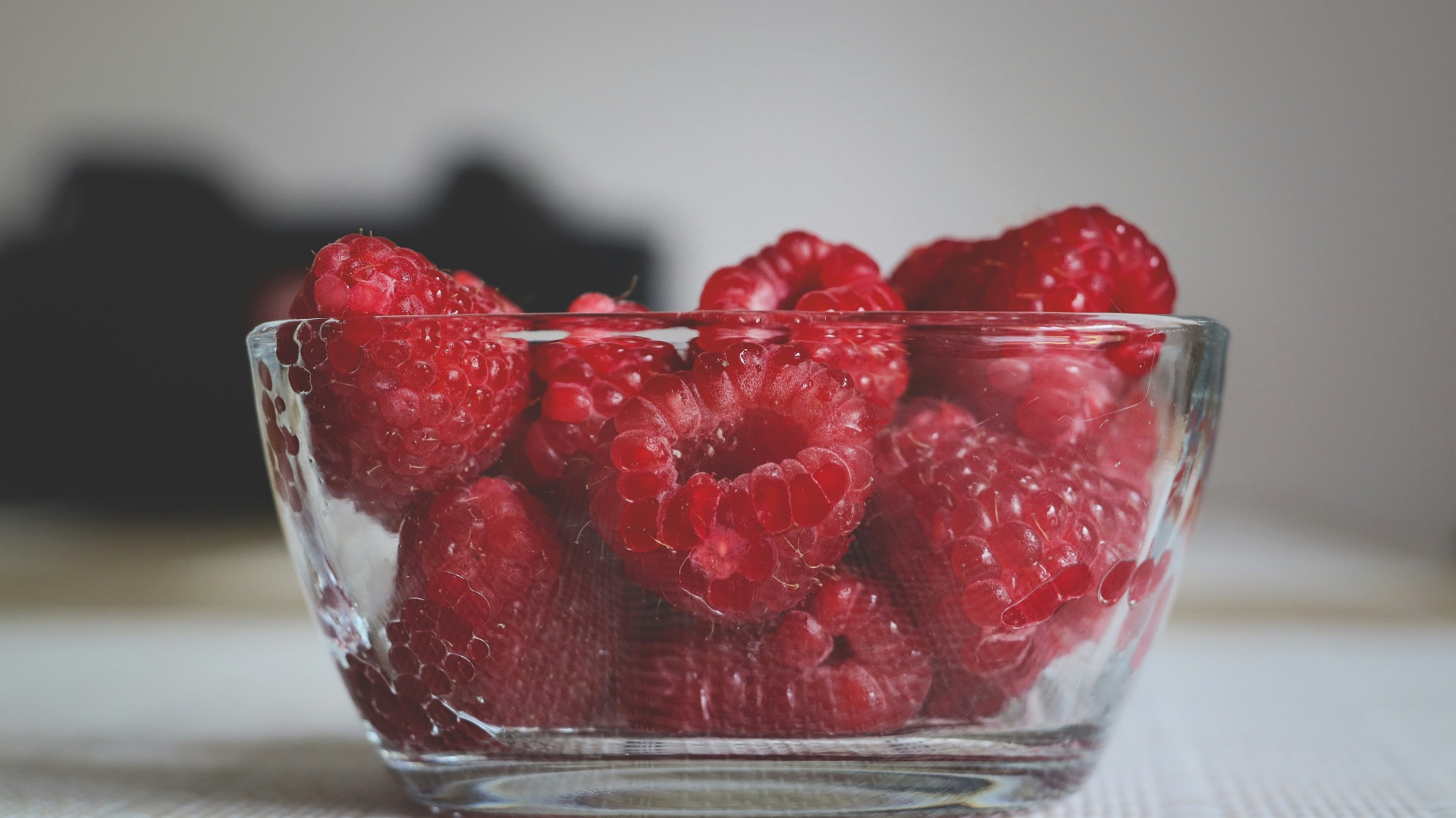 a glass bowl filled with raspberries on top of a table
