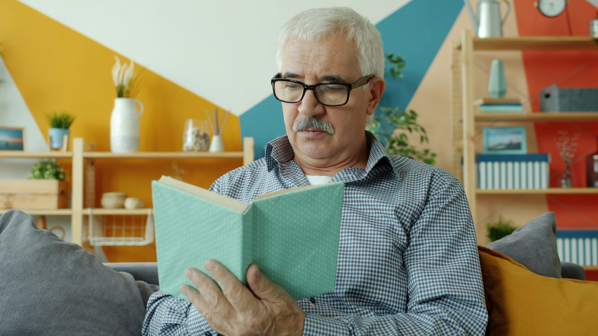 An elderly man with glasses reading a book.