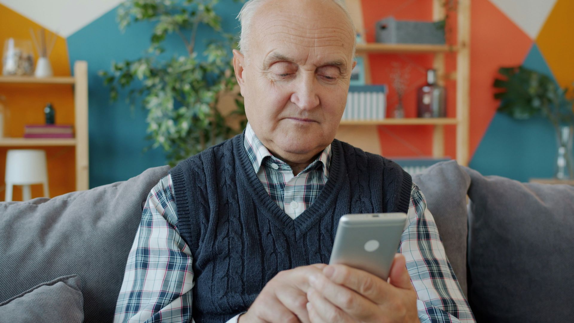 Elderly man using a smartphone on a couch.